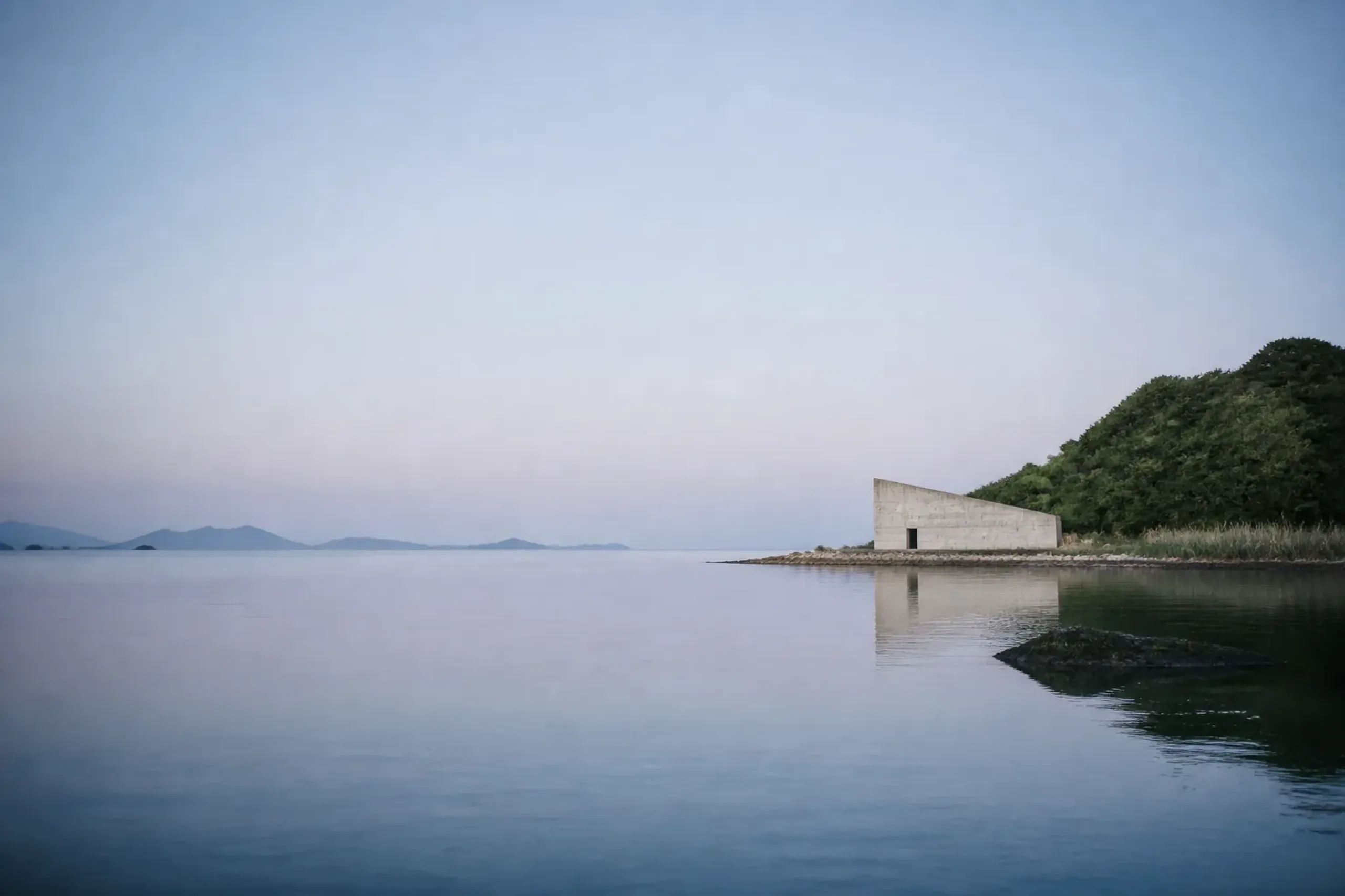 Quiet Naoshima coastline with calm sea and minimal architecture in the distance