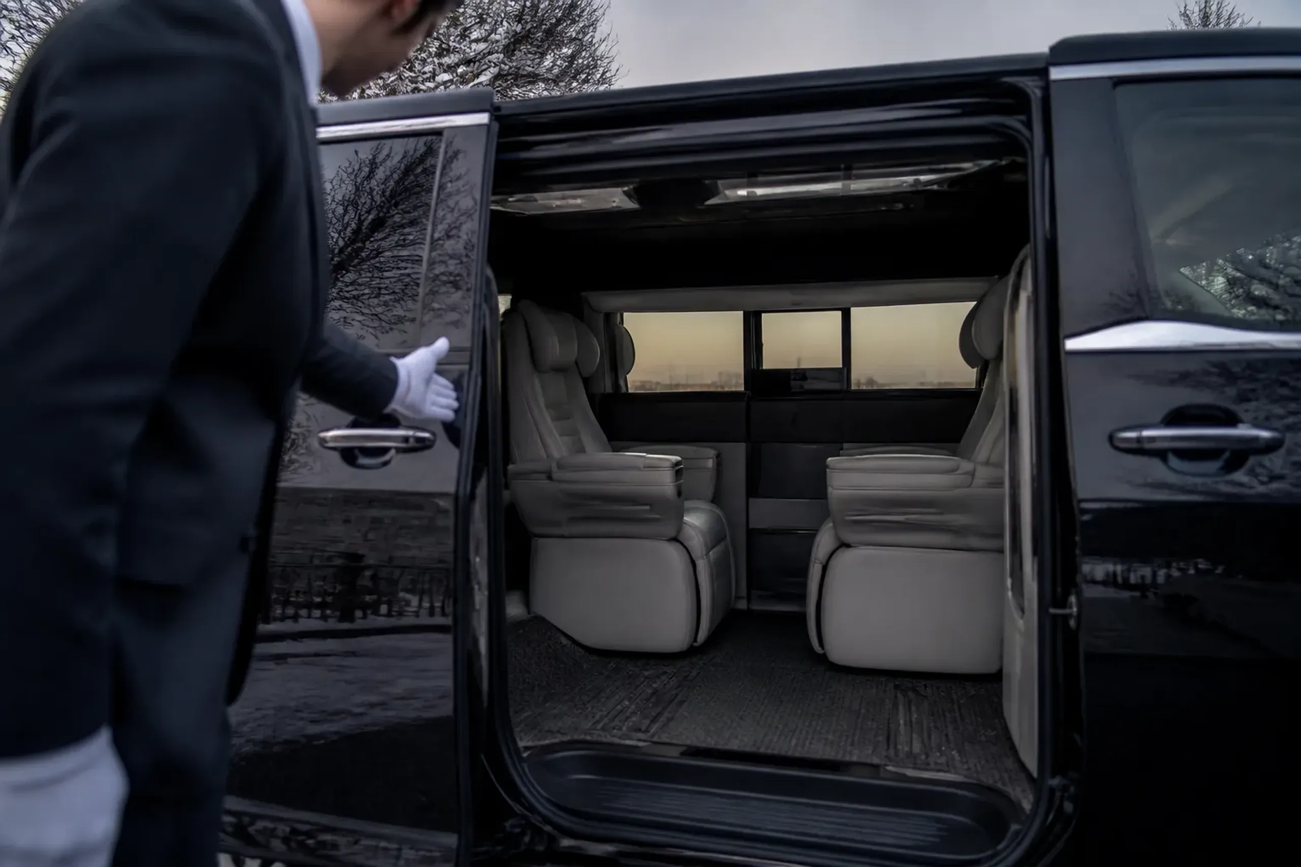 Cream leather reclining seats inside a Lexus LM 500 luxury minivan with a chauffeur opening the door