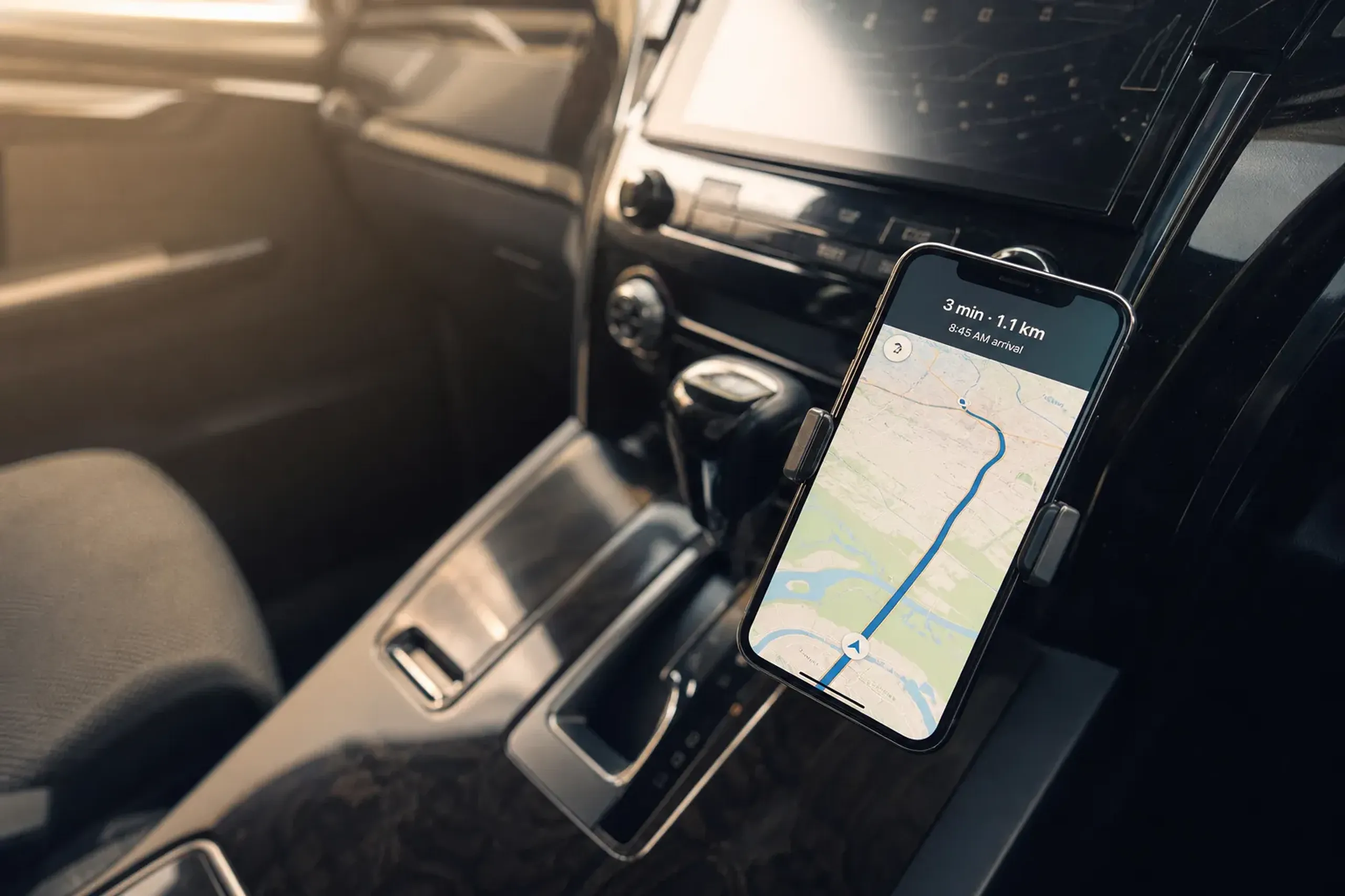A smartphone screen mounted in a car cradle displaying a live map with a driver's ETA and real-time route line, the Alphard dashboard blurred behind it