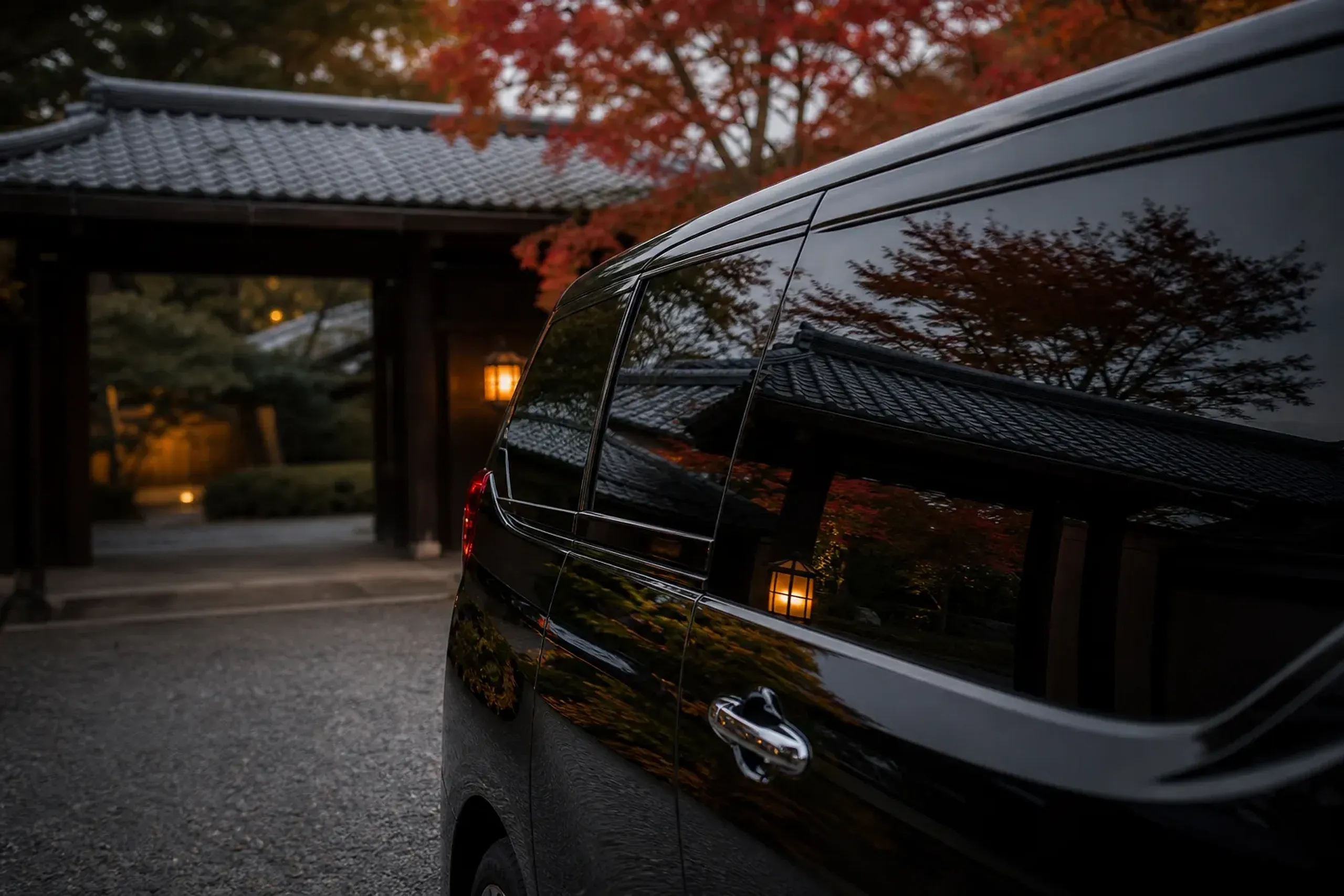 The tinted rear window of a black Alphard reflecting a traditional ryokan gateway, its interior cabin private and unseen
