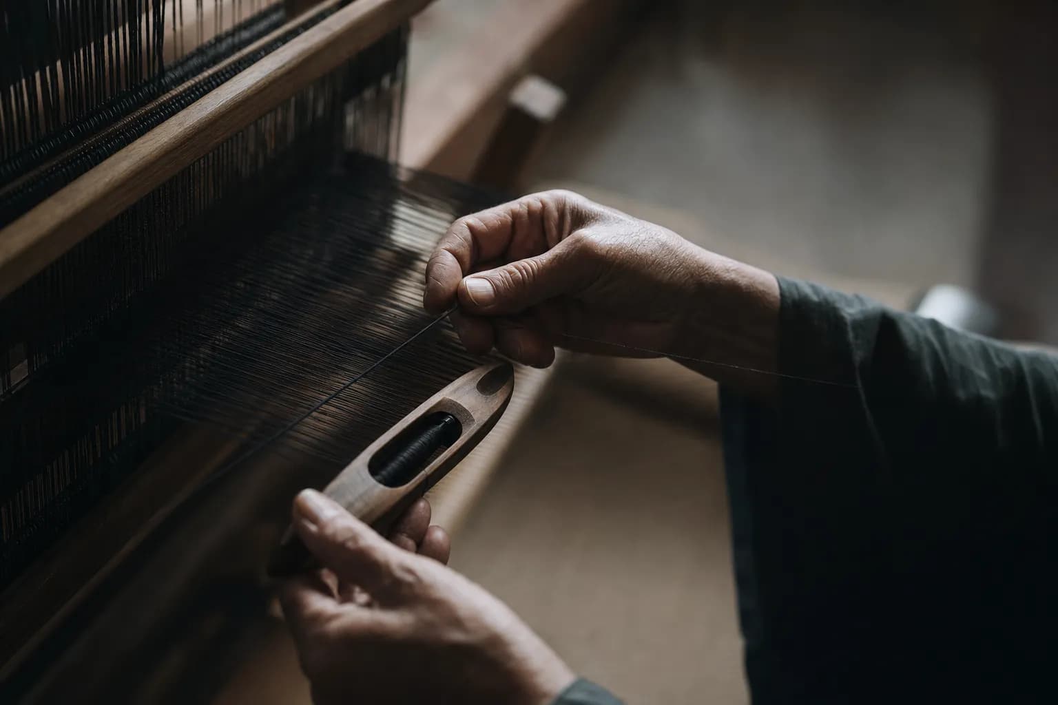 Artisan hands weaving deep black mud-dyed Oshima Tsumugi silk on a traditional loom