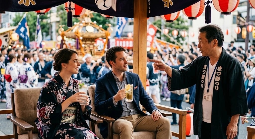 A couple seated under a festival booth drinks while a man in traditional attire points and talks to them, with a crowded street festival behind.