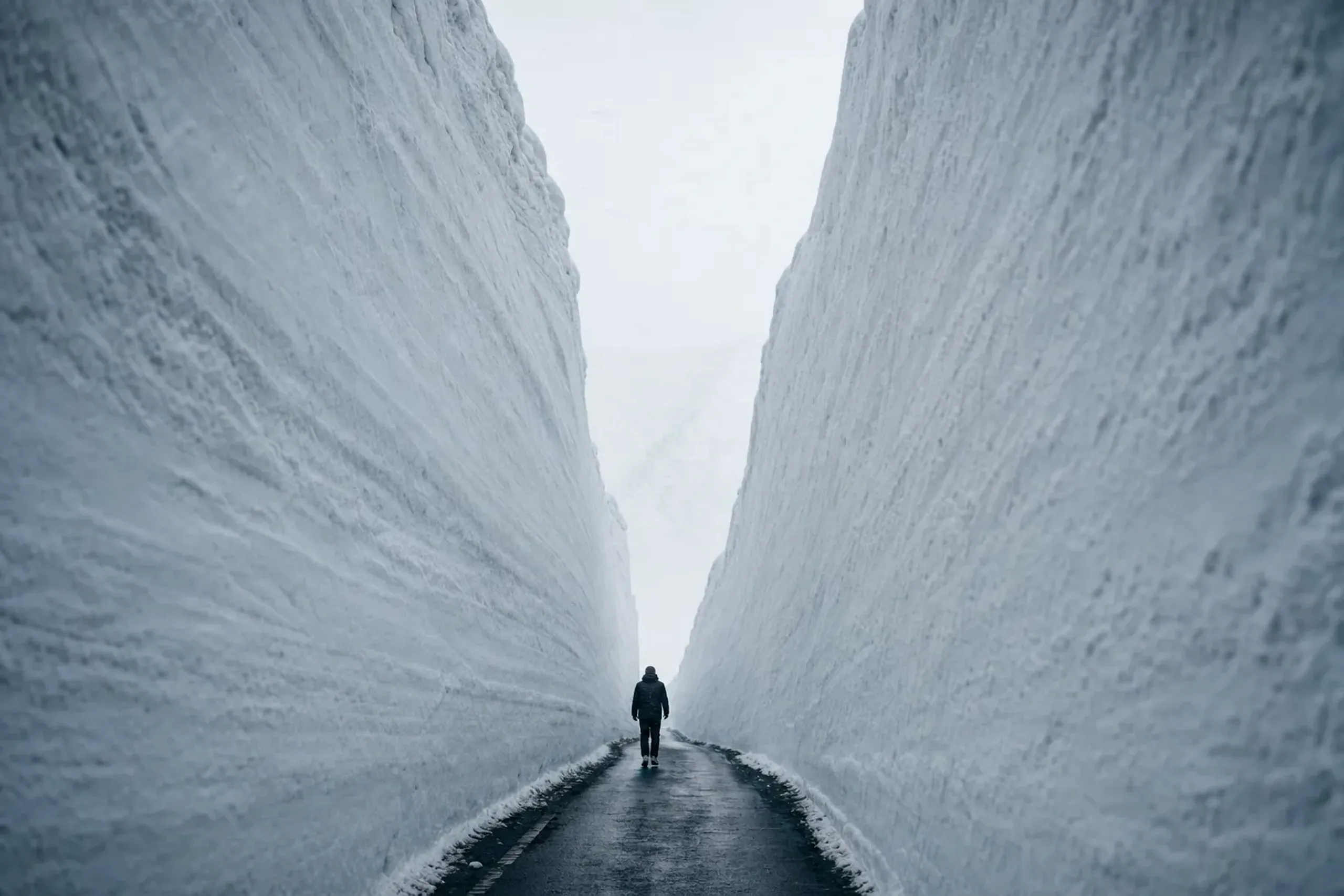 The plowed snow corridor along National Route 103 near Kasamatsu Pass, with sawed vertical snow walls rising roughly 7 meters above a narrow ribbon of asphalt at around 1,040 meters elevation