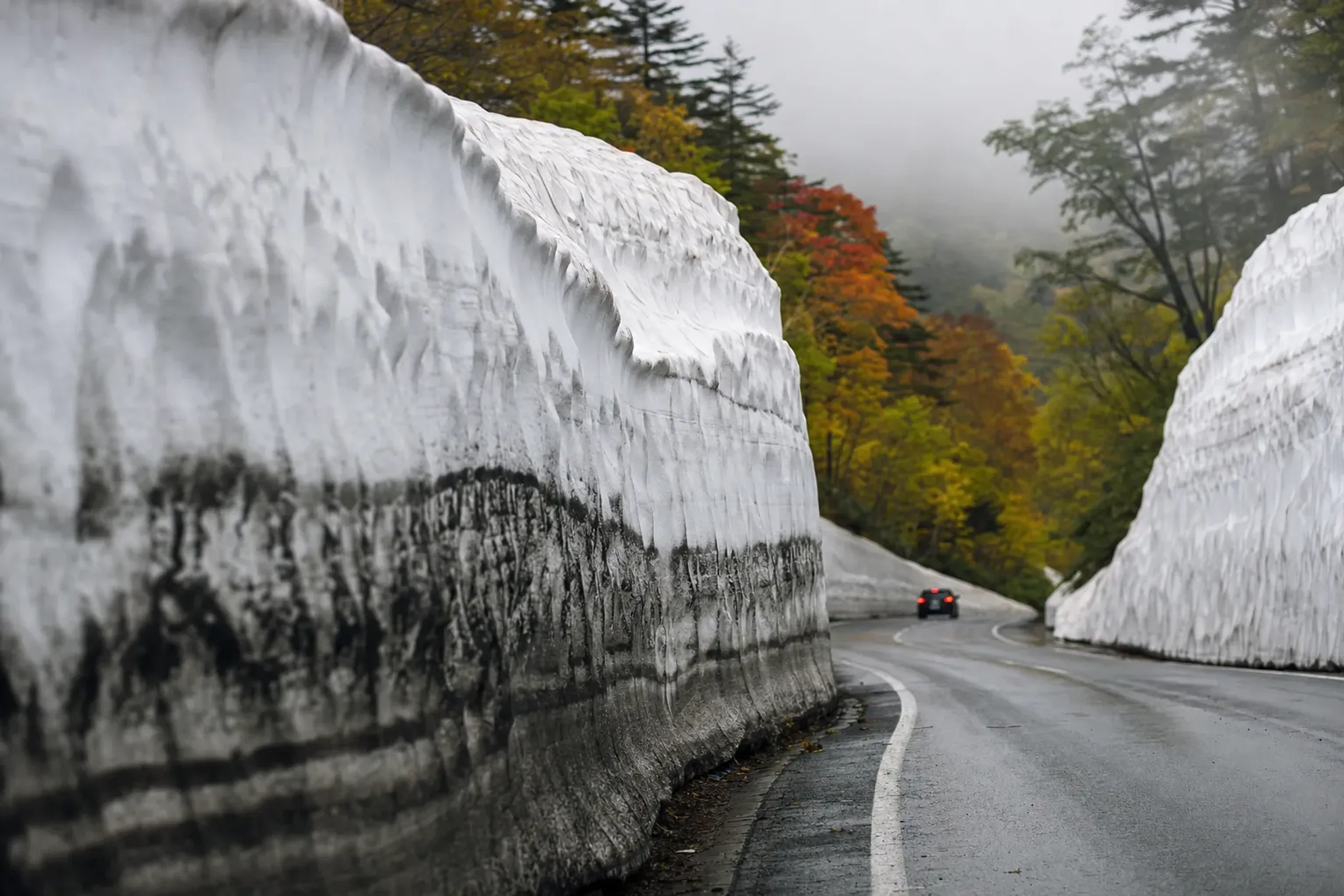 The reopened Hakkōda-Towada Gold Line snow corridor stretch on the Sukayu side near the Hakkōda Hotel, its packed white walls edged by grimy exhaust-darkened snow