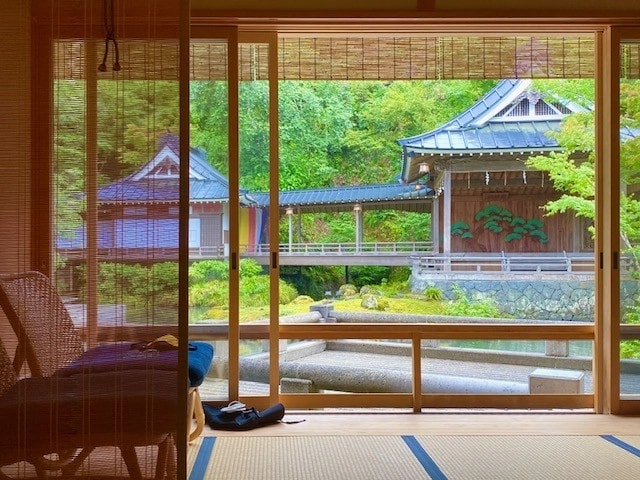 The Gekkeiden Noh stage glowing with stage lights at dusk, reflected on the dark surface of Asaba Ryokan's central pond with its calligraphic roofline against the trees