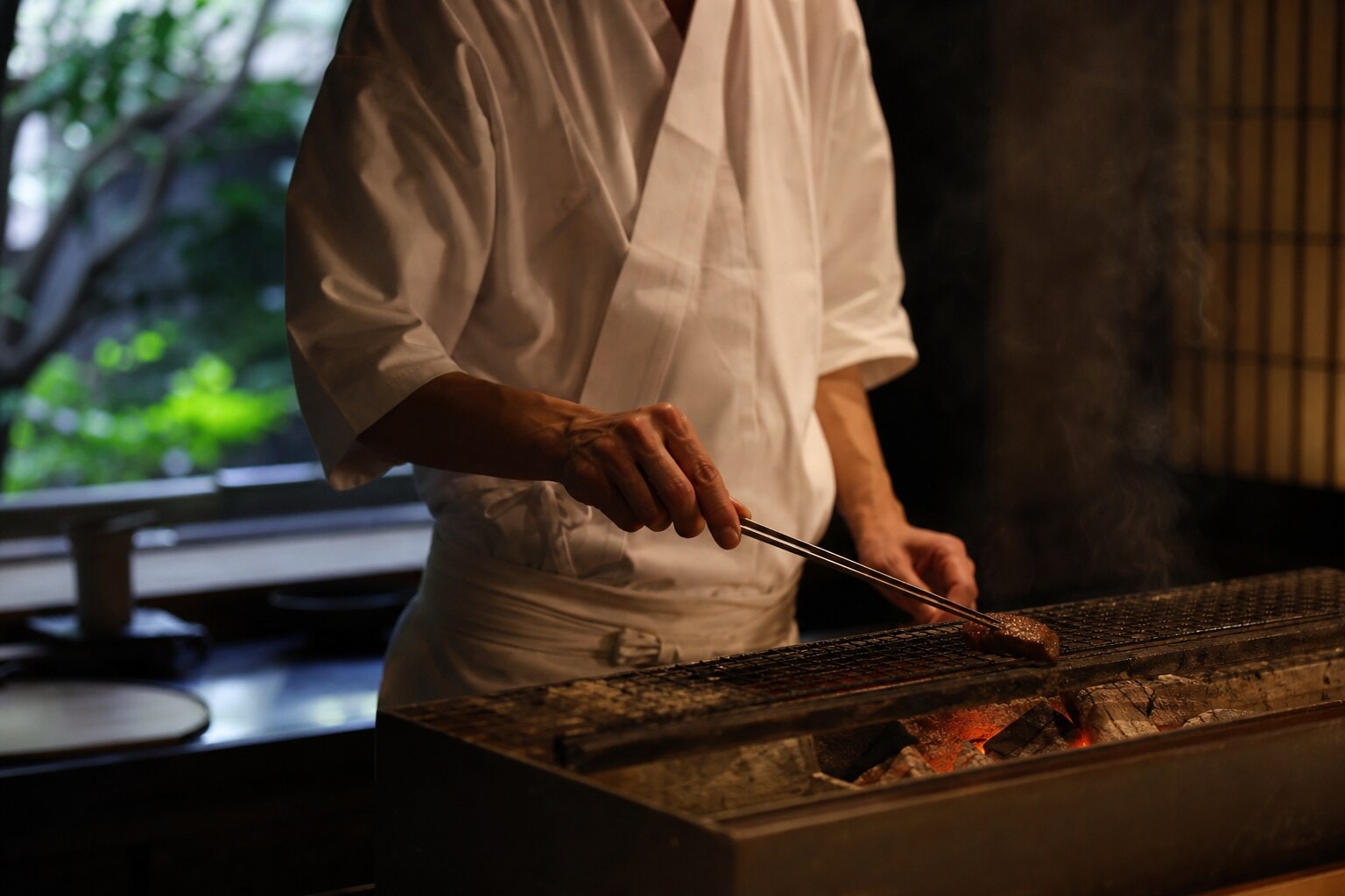 Japanese chef carefully grilling a piece of premium beef over glowing charcoal