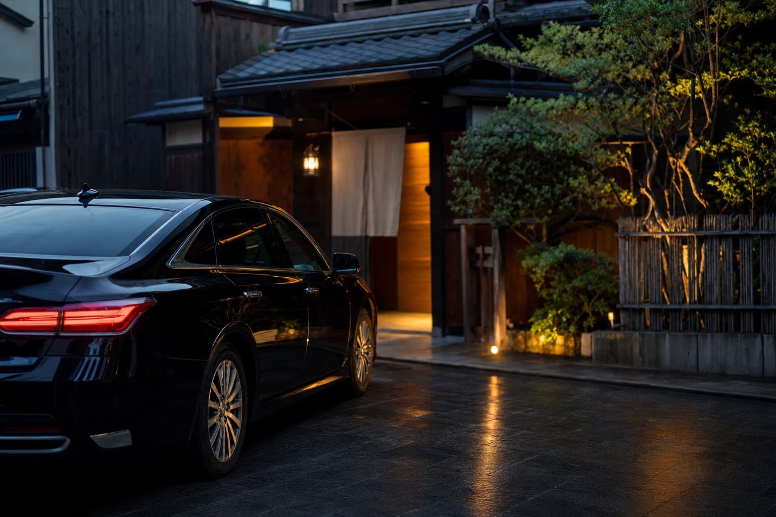 Black luxury chauffeur vehicle parked outside a traditional Japanese restaurant at dusk
