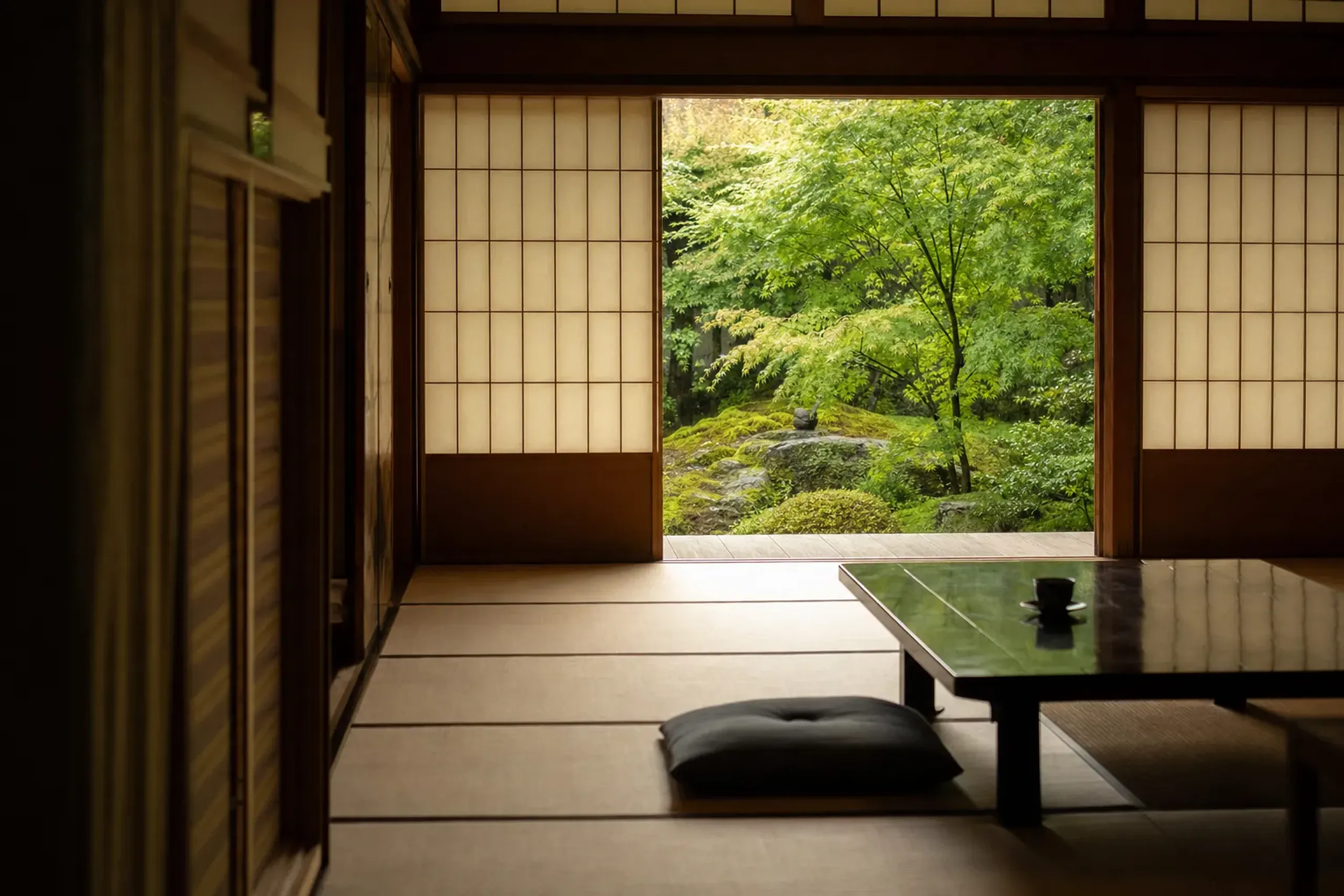 Minimalist tatami ryokan room with timber and paper screens framing a garden view