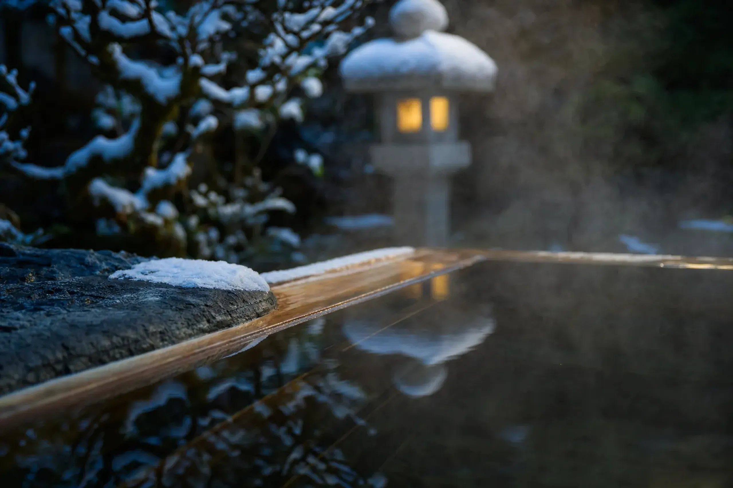 Steaming private open-air onsen bath of wood and stone in a quiet winter garden