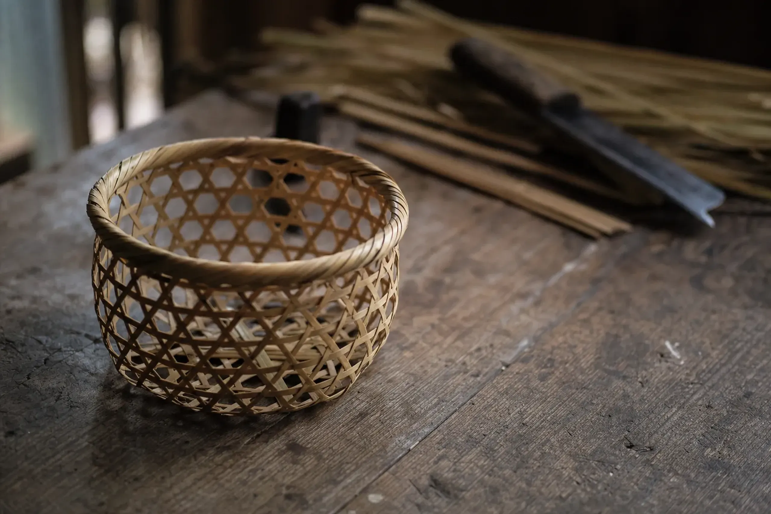 A precise, delicately woven Beppu bamboo basket resting on a raw timber workbench in a shokunin's workshop