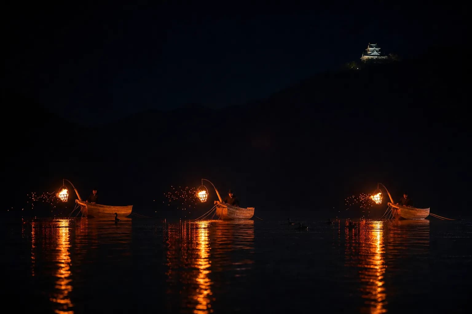 Night cormorant fishing boats with fire baskets on the Nagara River below illuminated Gifu Castle