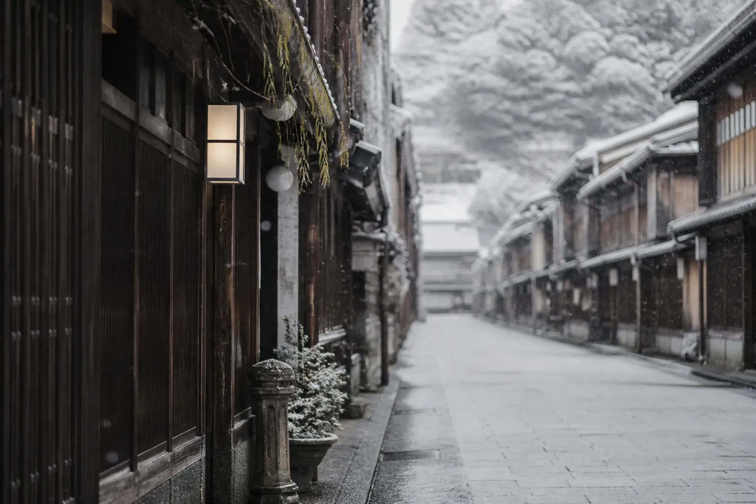Snow falling on a preserved Kanazawa street of dark wooden townhouses in soft winter light