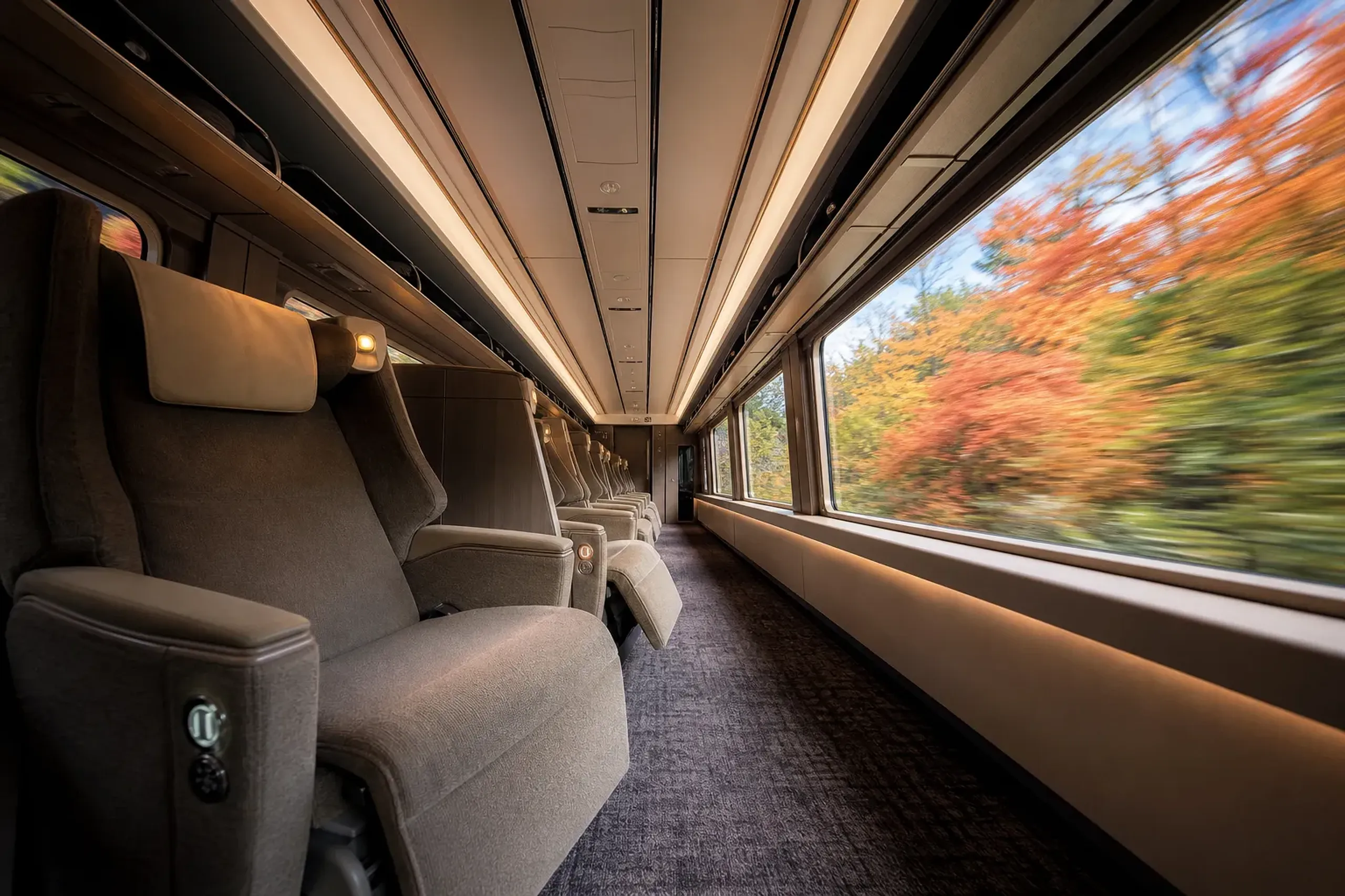 the interior of a green-car shinkansen carriage with reclining seats and large windows revealing the passing countryside
