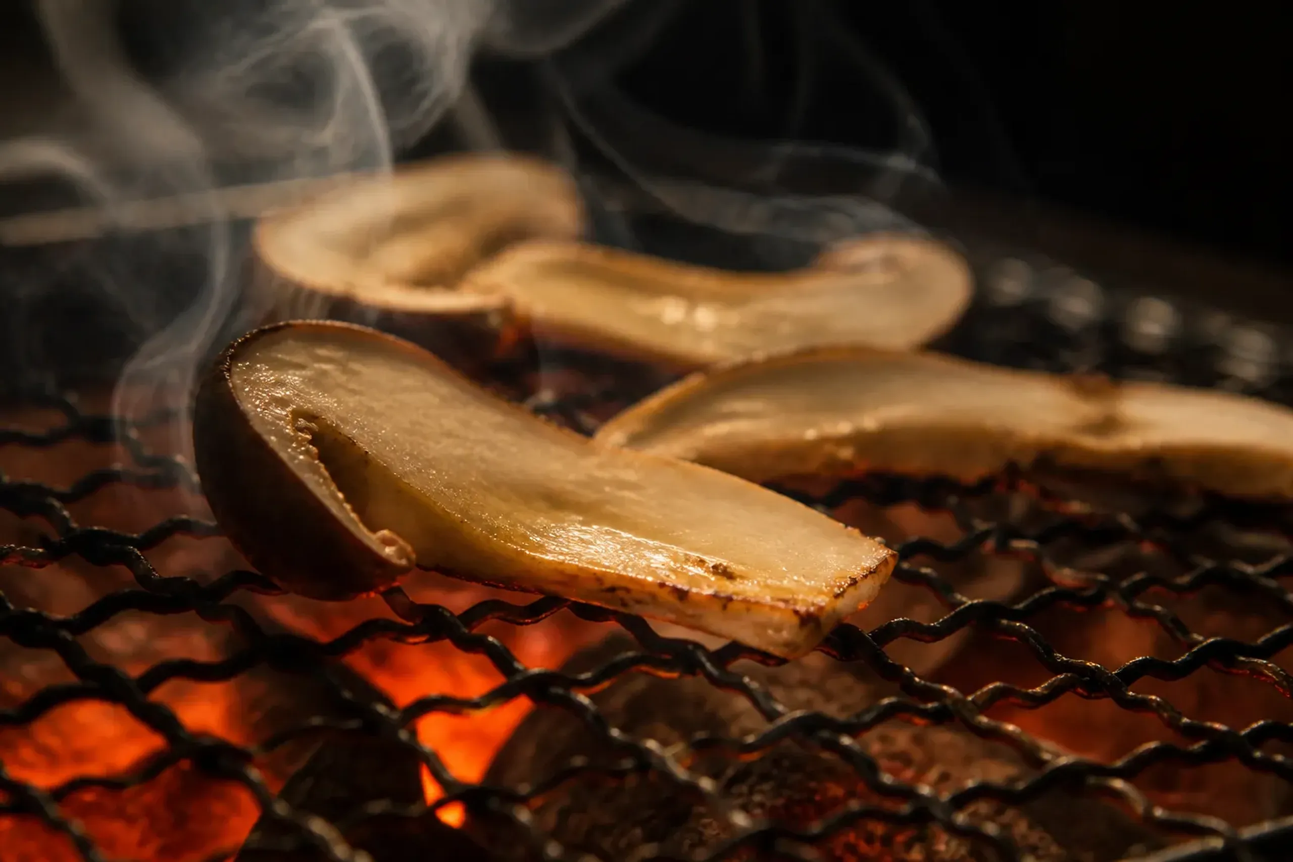 a thin-sliced wild matsutake mushroom barely seared over a charcoal grill in a traditional Japanese kitchen, its pale cap and thick stem glistening, prepared as the meal built around the day's hunt