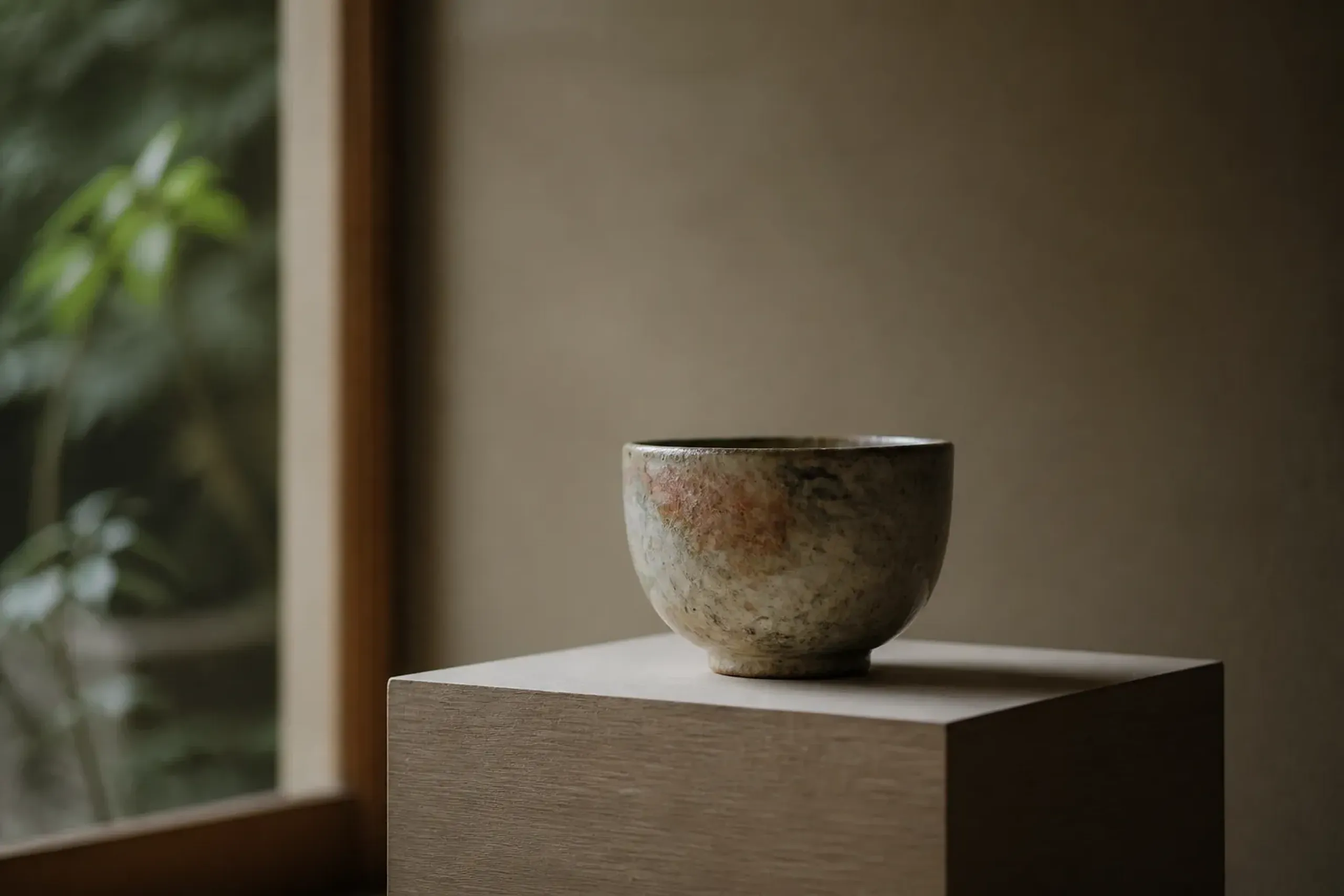 a collector-grade kogei ceramic tea bowl with a subtly glazed, wabi-sabi surface displayed on a plain wooden pedestal in soft daylight, showing material truth and lineage rather than ornamentation
