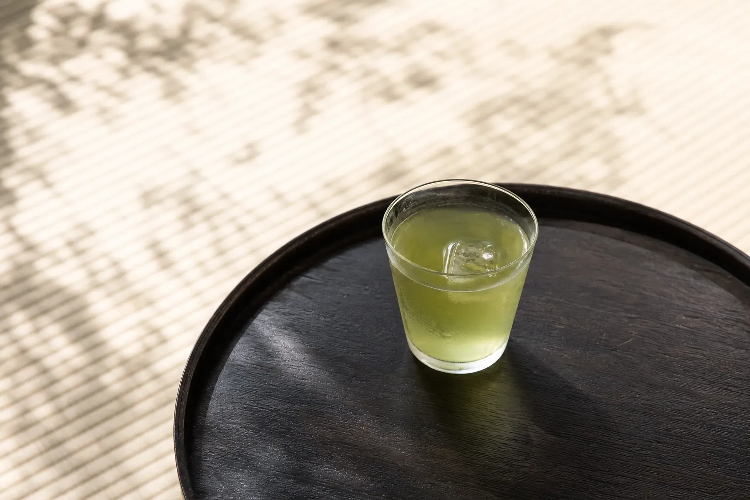 Pale jade cold-brew gyokuro tea served in a small glass on a wooden tray in a Japanese tea room