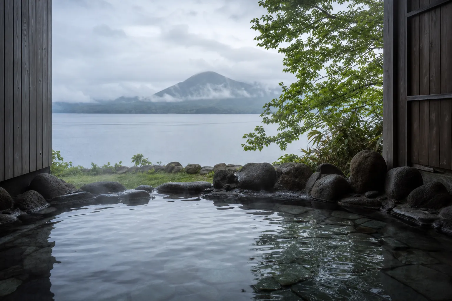 Open-air stone onsen bath overlooking Lake Shikotsu surrounded by autumn forest