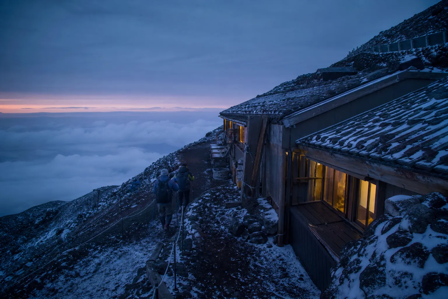 A mountain hut high on Mount Fuji’s slope with hikers arriving on volcanic terrain