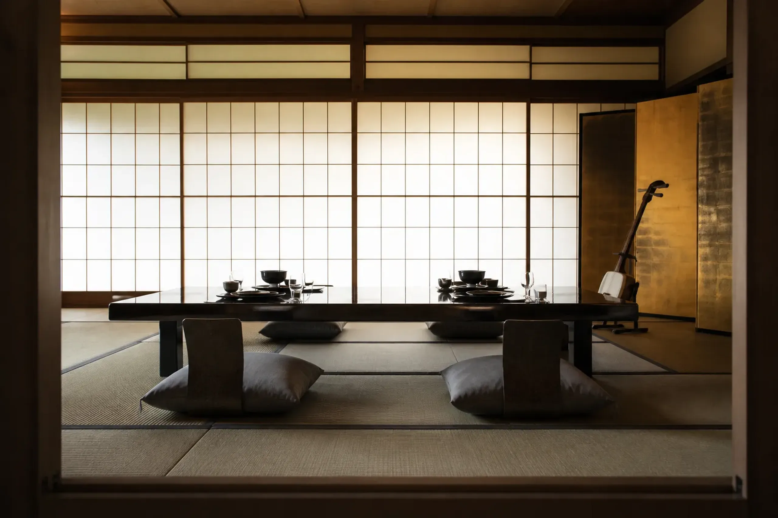 A private tatami room set for an Asakusa ozashiki banquet, with a low lacquered table arranged for kaiseki cuisine, a shamisen resting on its stand, and folding gold screens against sliding shoji door