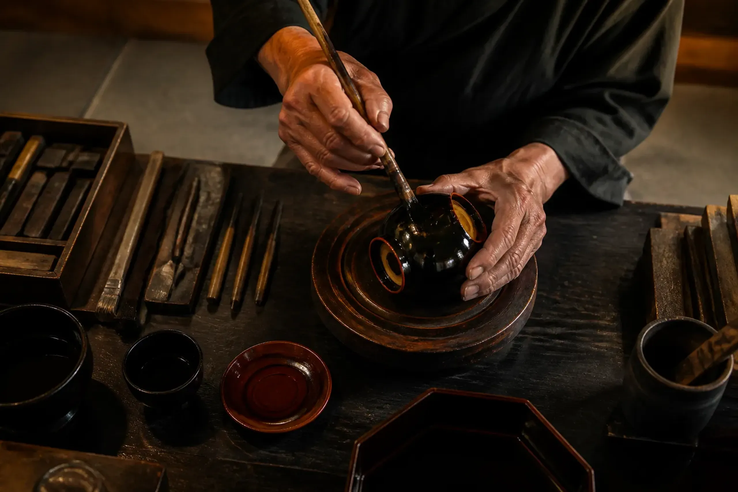 Artisan hands working at a wooden bench with traditional tools in soft light