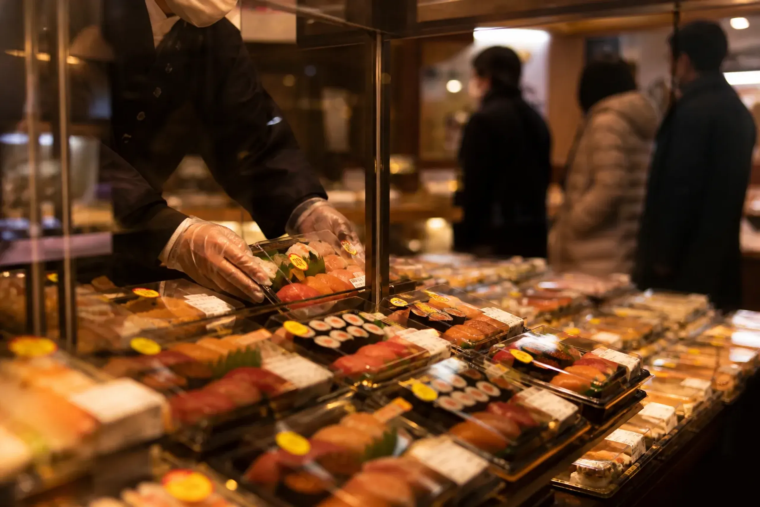 Prepared foods in depachika with discount stickers as staff restock behind glass