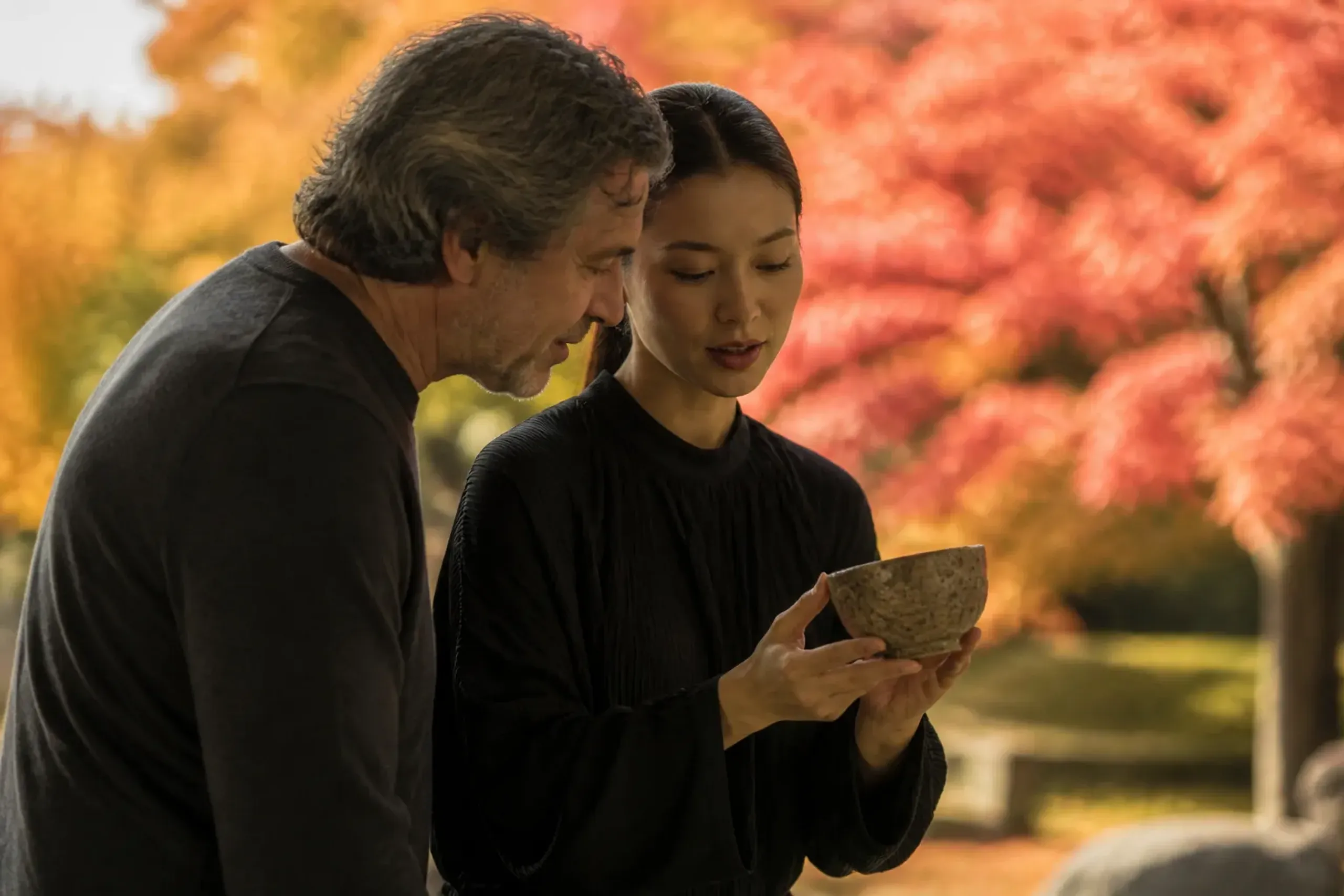 A collector in conversation with a young Japanese designer beside a contemporary object in a quiet Tokyo gallery