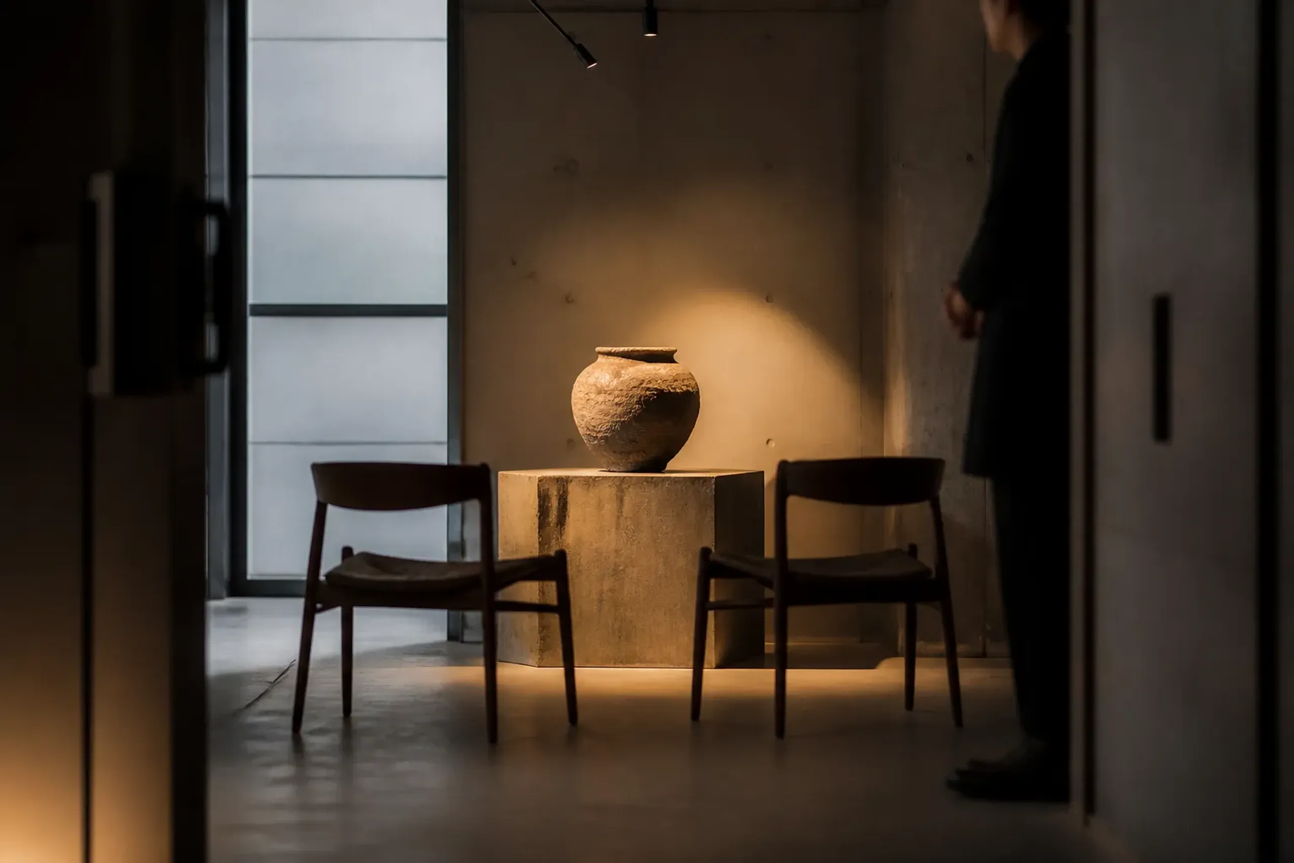 a single unglazed ceramic vessel with iron-speckled clay on a raw plaster shelf in a converted Aoyama shopfront, lit only by the low autumn sun through the window