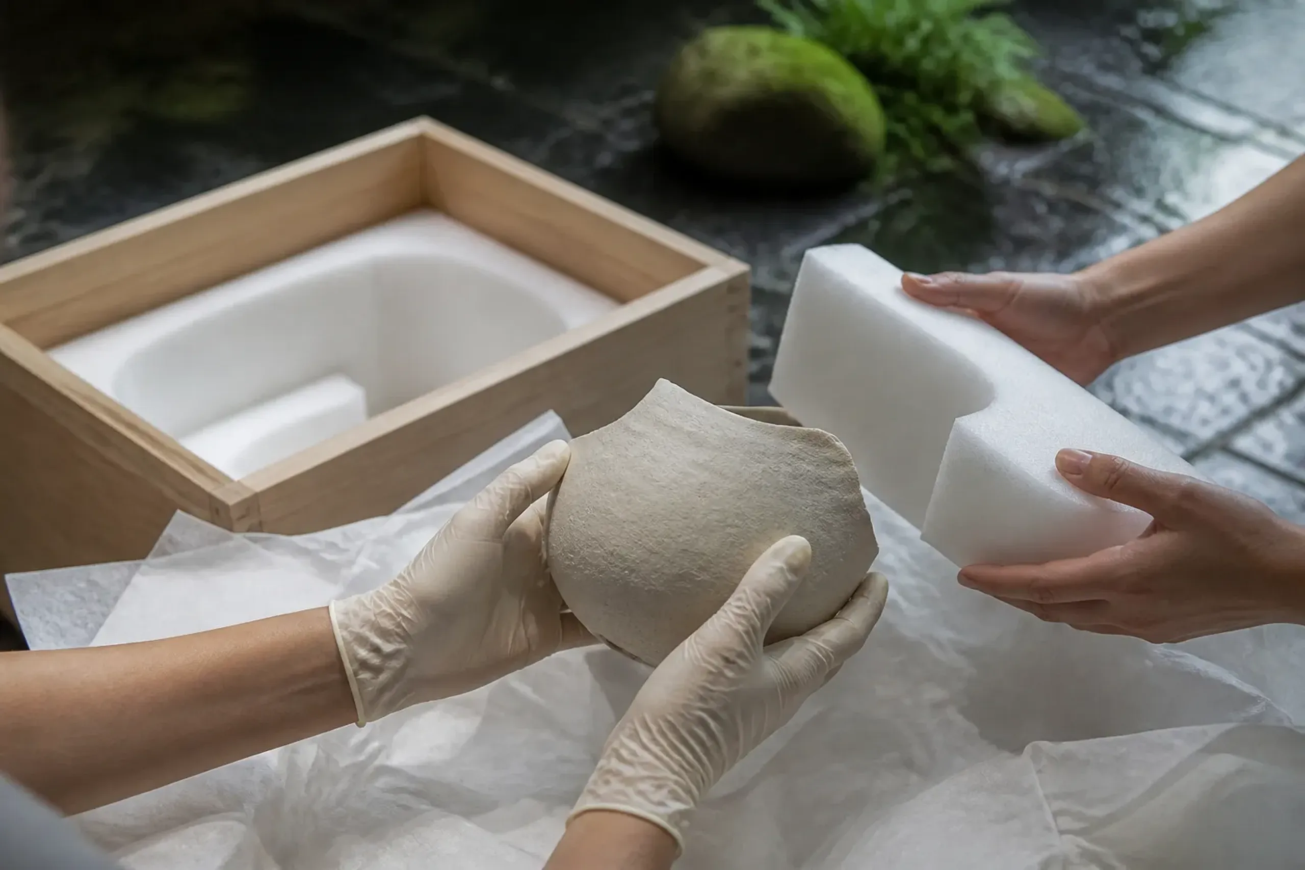 Gloved hands building a custom wooden crate around a lacquer panel with export documents on a workbench