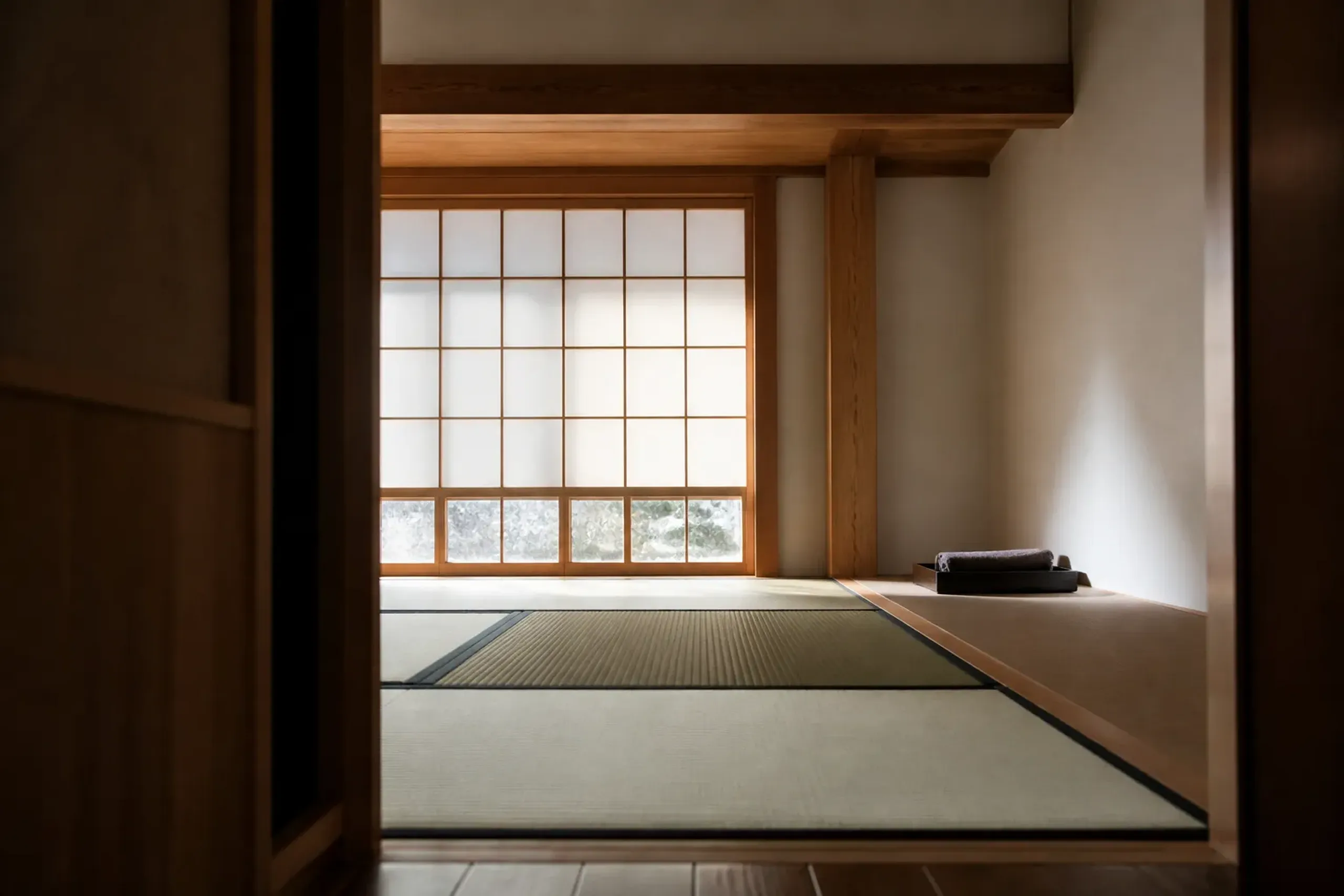 A newly finished ryokan guest room interior with untouched fresh tatami mats, crisp white plaster walls, and pale unblemished timber beams catching soft morning light