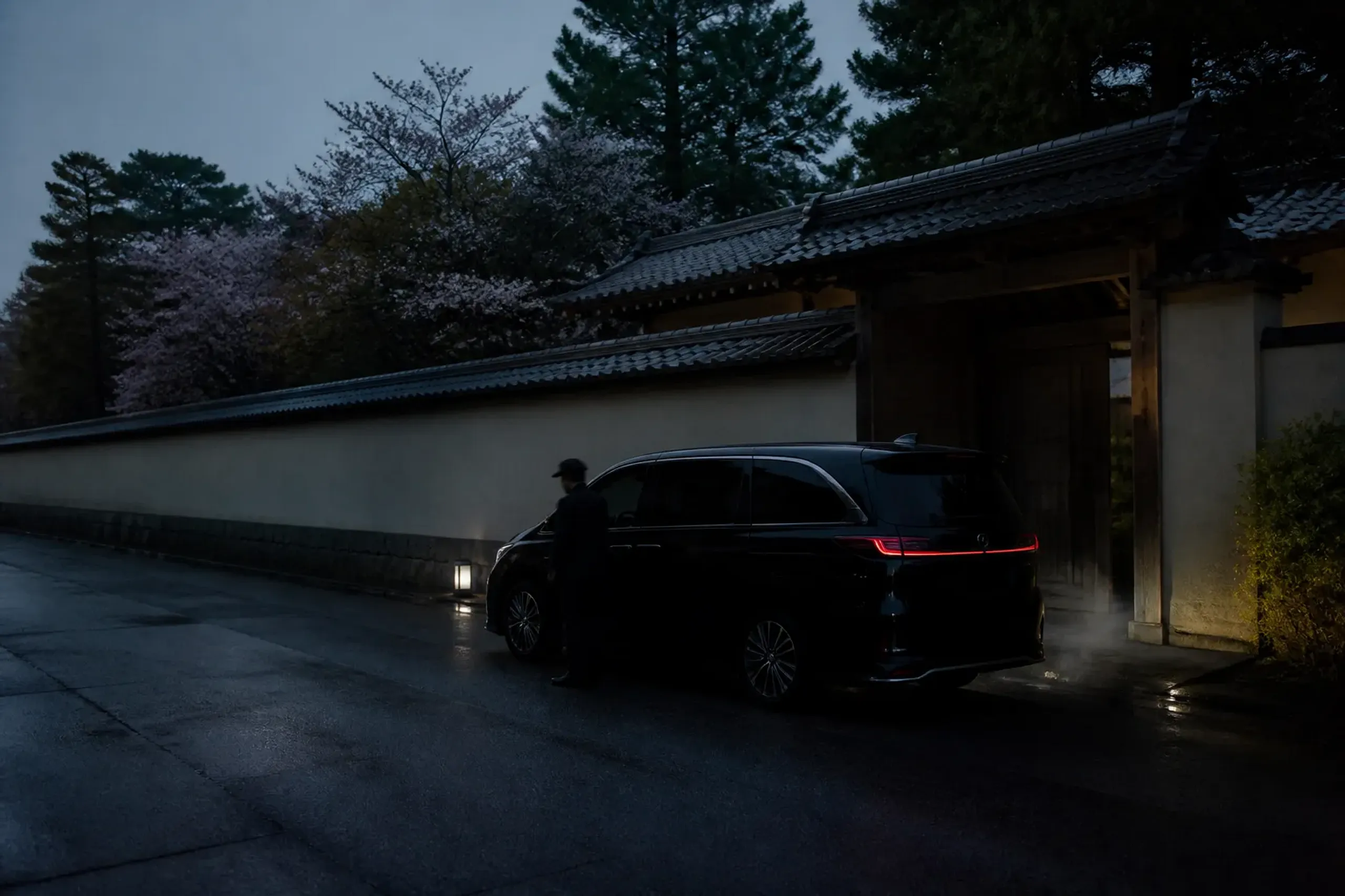 a single black chauffeured Lexus LM 500 idling at a discreet side entrance of a Kyoto hotel at dawn, its screened rear cabin darkened, empty pavement stretching ahead in soft early light