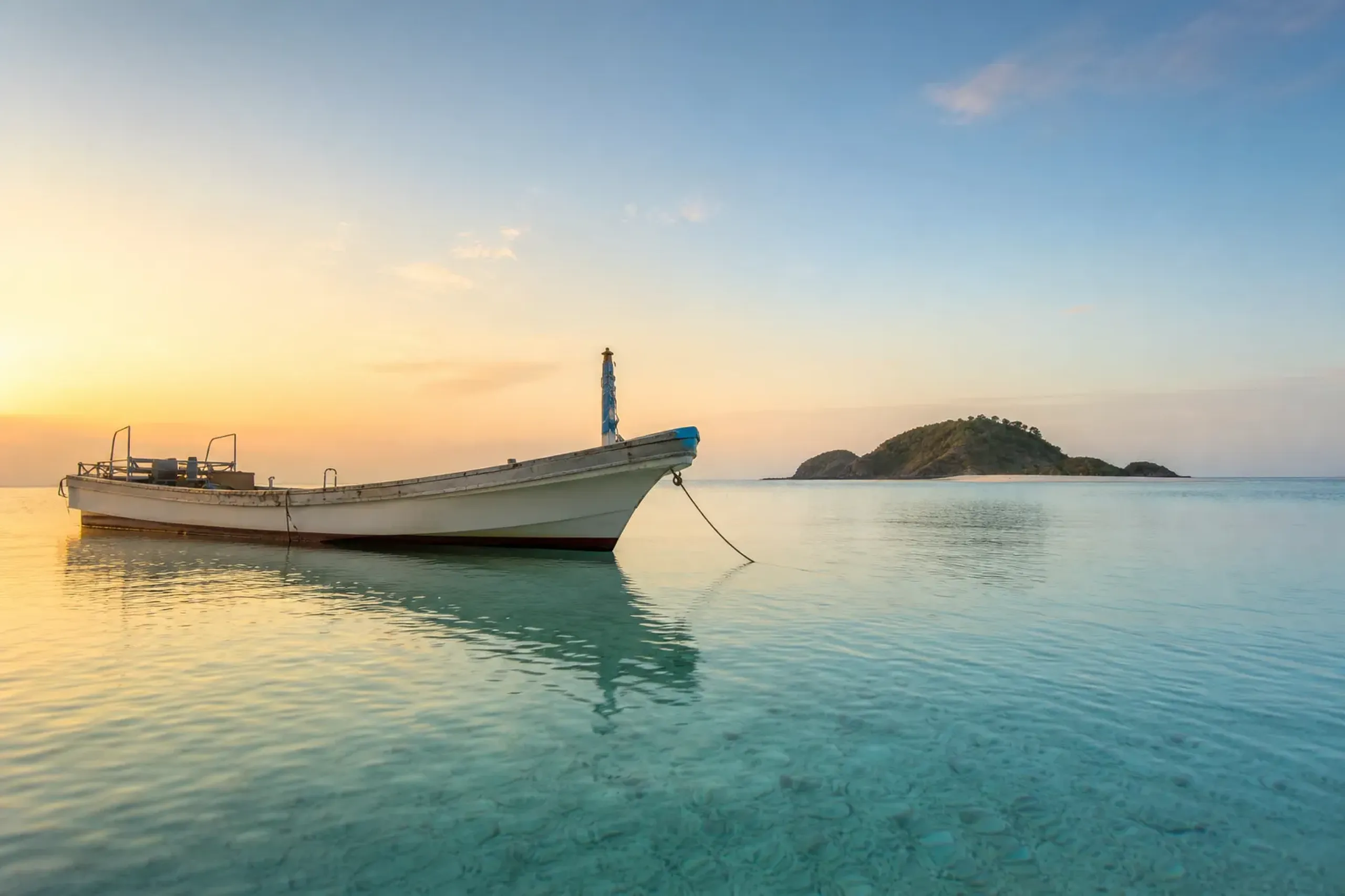 Small private dive boat in calm water near an uninhabited Kerama islet at sunrise