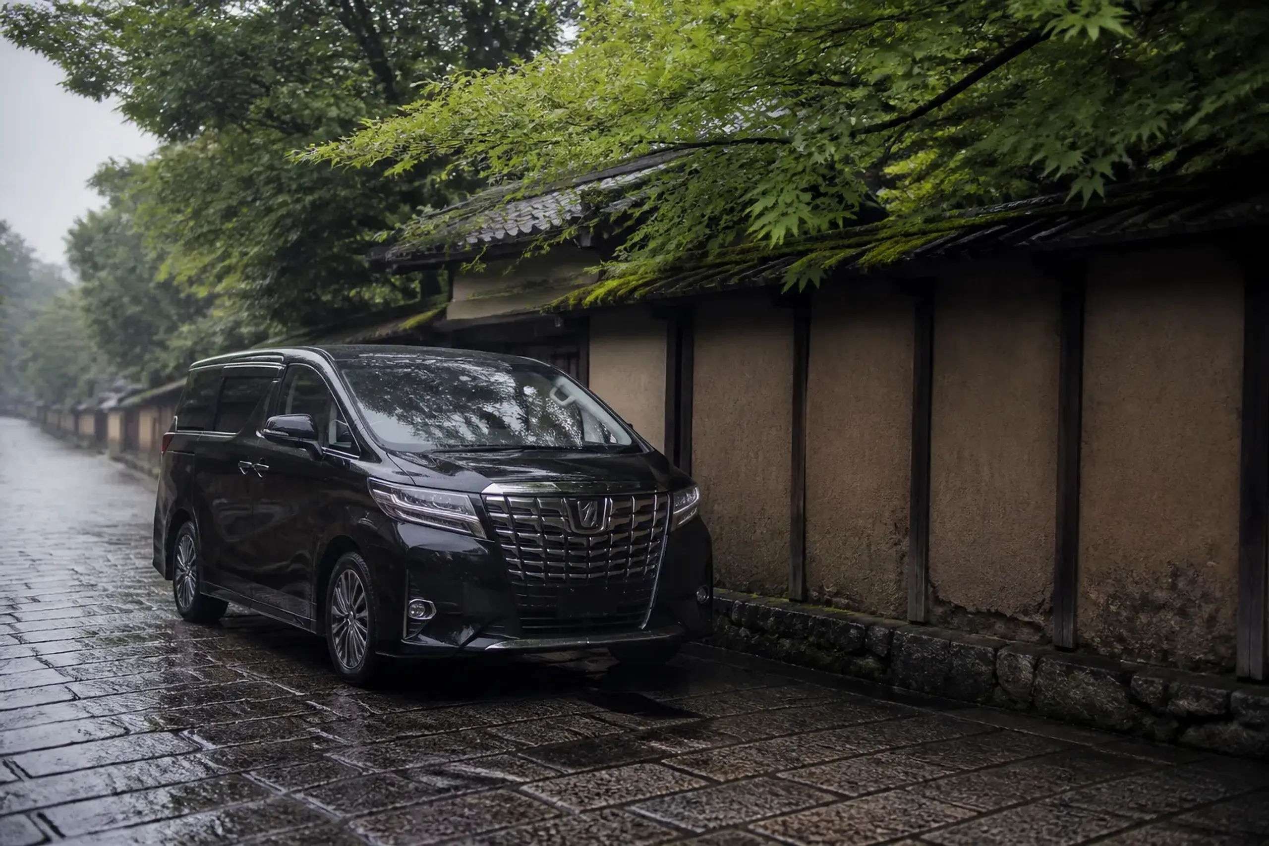 Black luxury minivan parked on a quiet Kyoto side street near traditional walls
