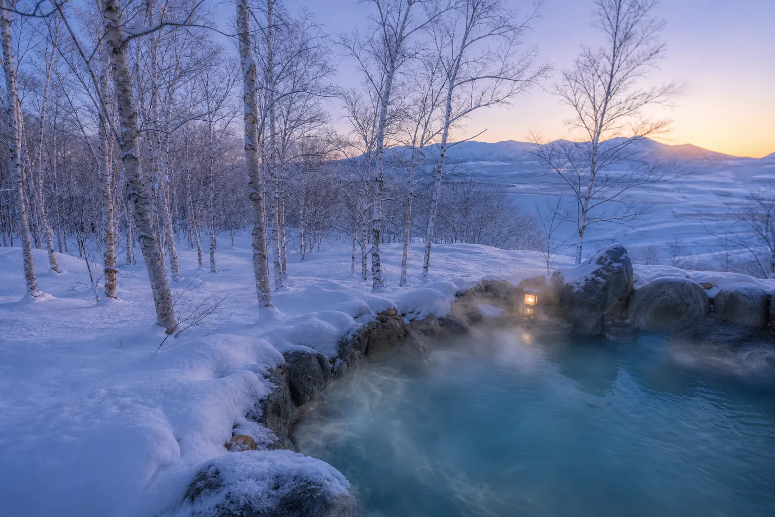 Steaming outdoor onsen surrounded by snow and birch trees near Furano in winter