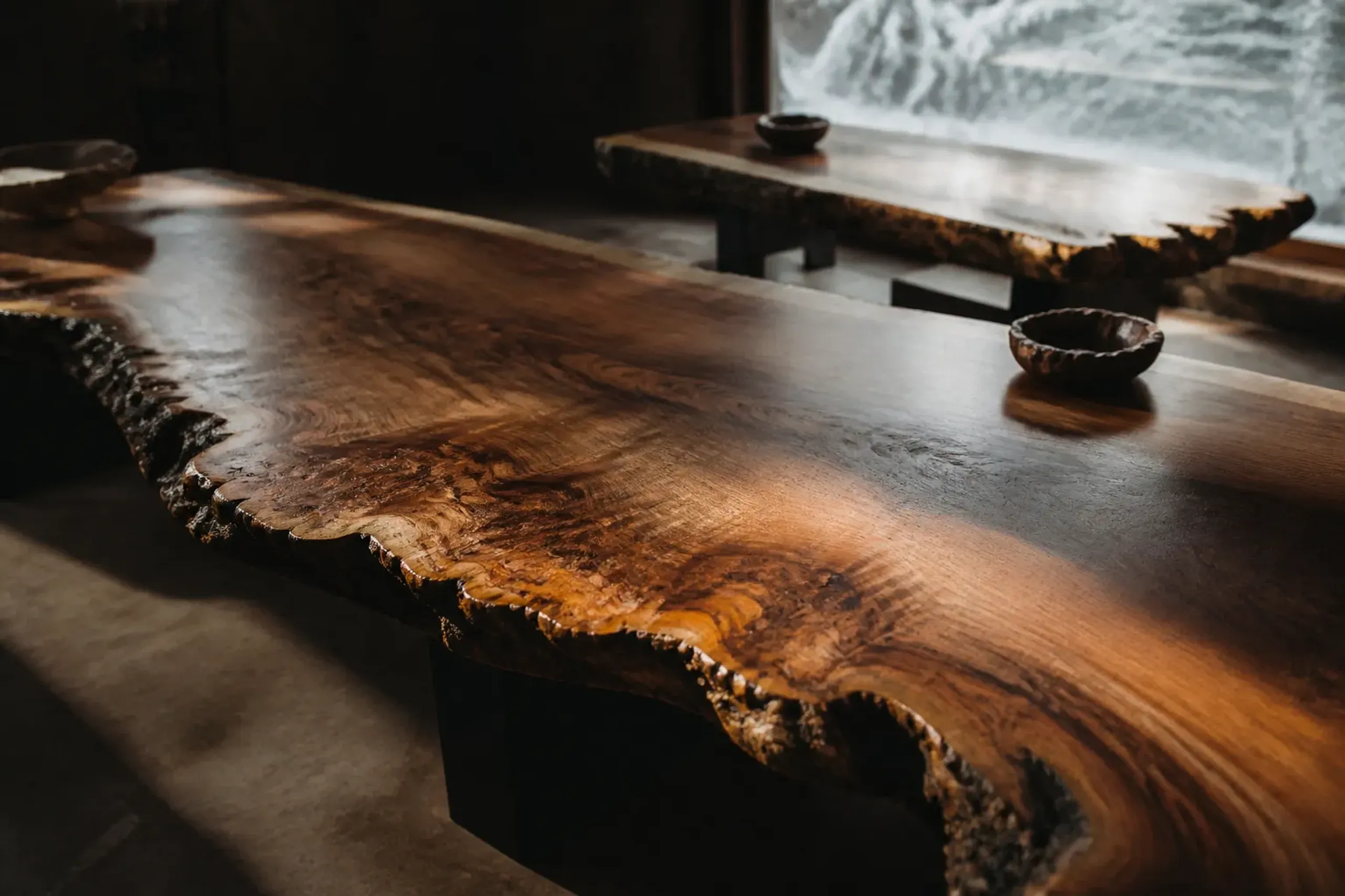 A first-floor gallery room at the Nakashima workshop in Mure filled with walnut studio furniture, lit for the tables rather than as a museum, each piece showing its natural free edge