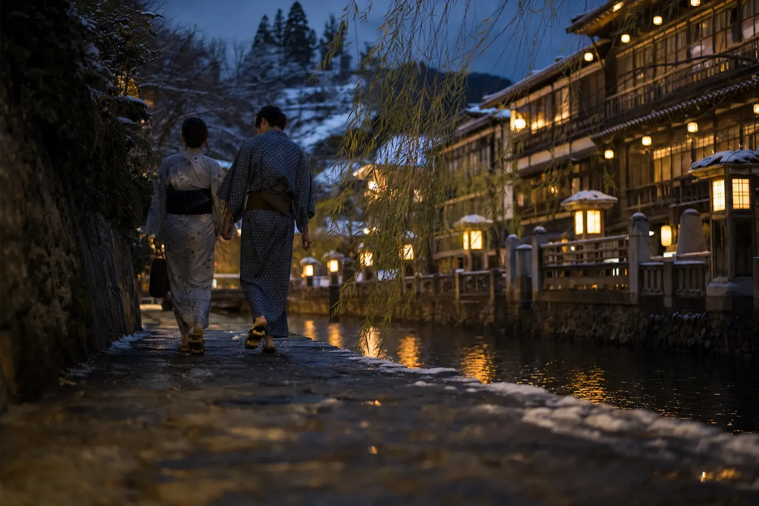 willow-lined lanes of Kinosaki at evening, wooden geta sandals and yukata-clad strollers walking between the town's public bathhouses as the lights come on