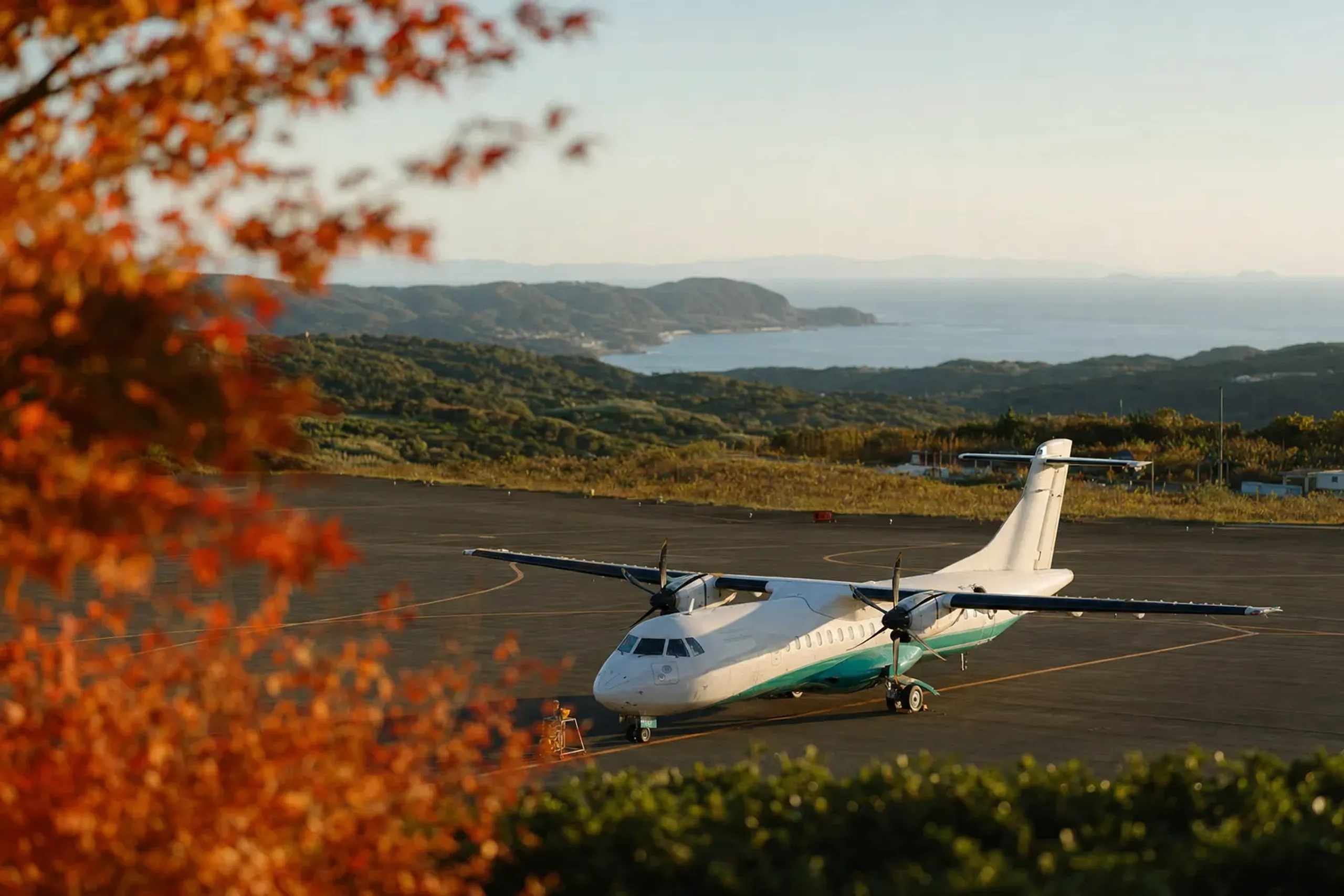 A small propeller aircraft on the tarmac at Fukue Airport with the island's green hills and coastline beyond