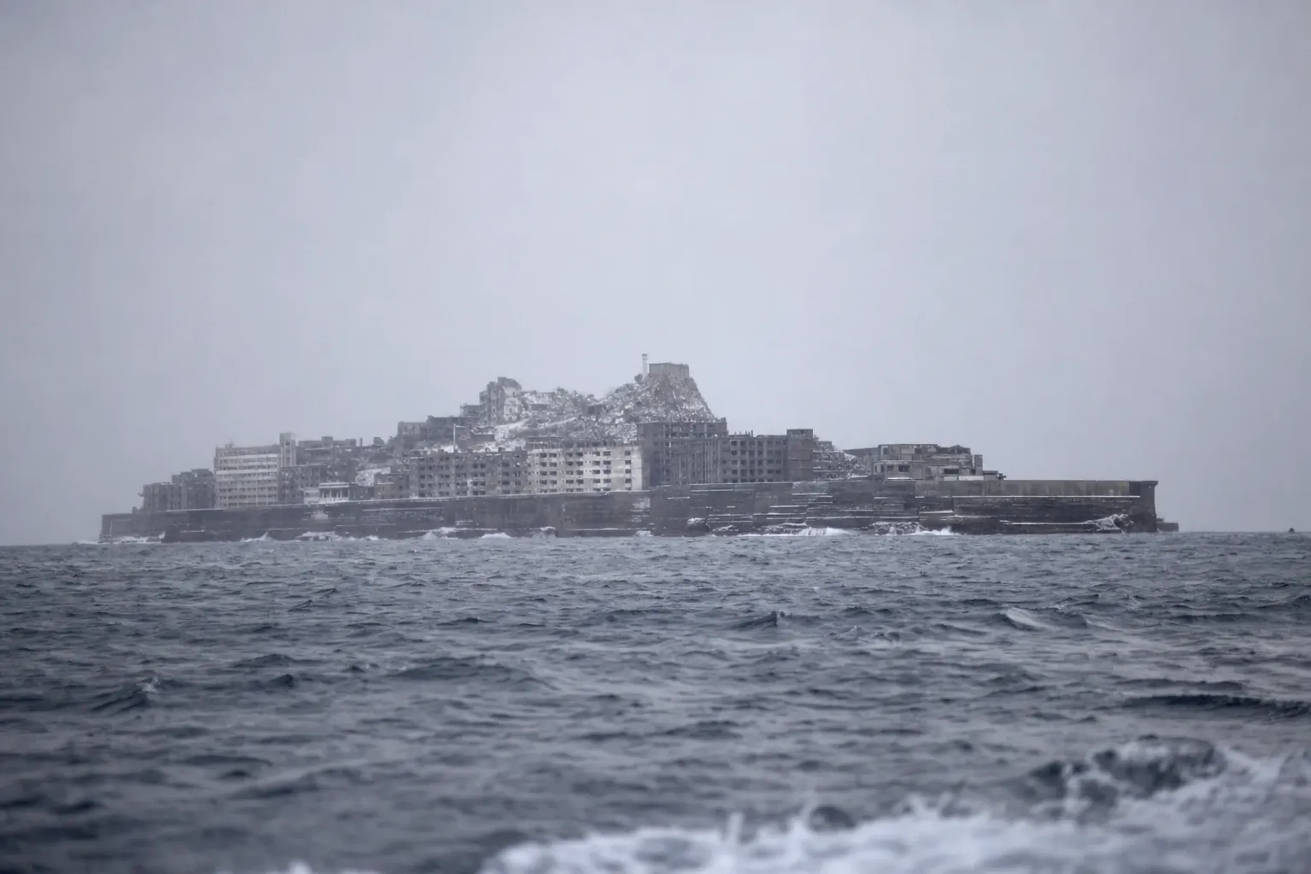 Hashima Island (Gunkanjima) seen from a tour boat, showing the seawalls and dense concrete buildings that create the battleship silhouette