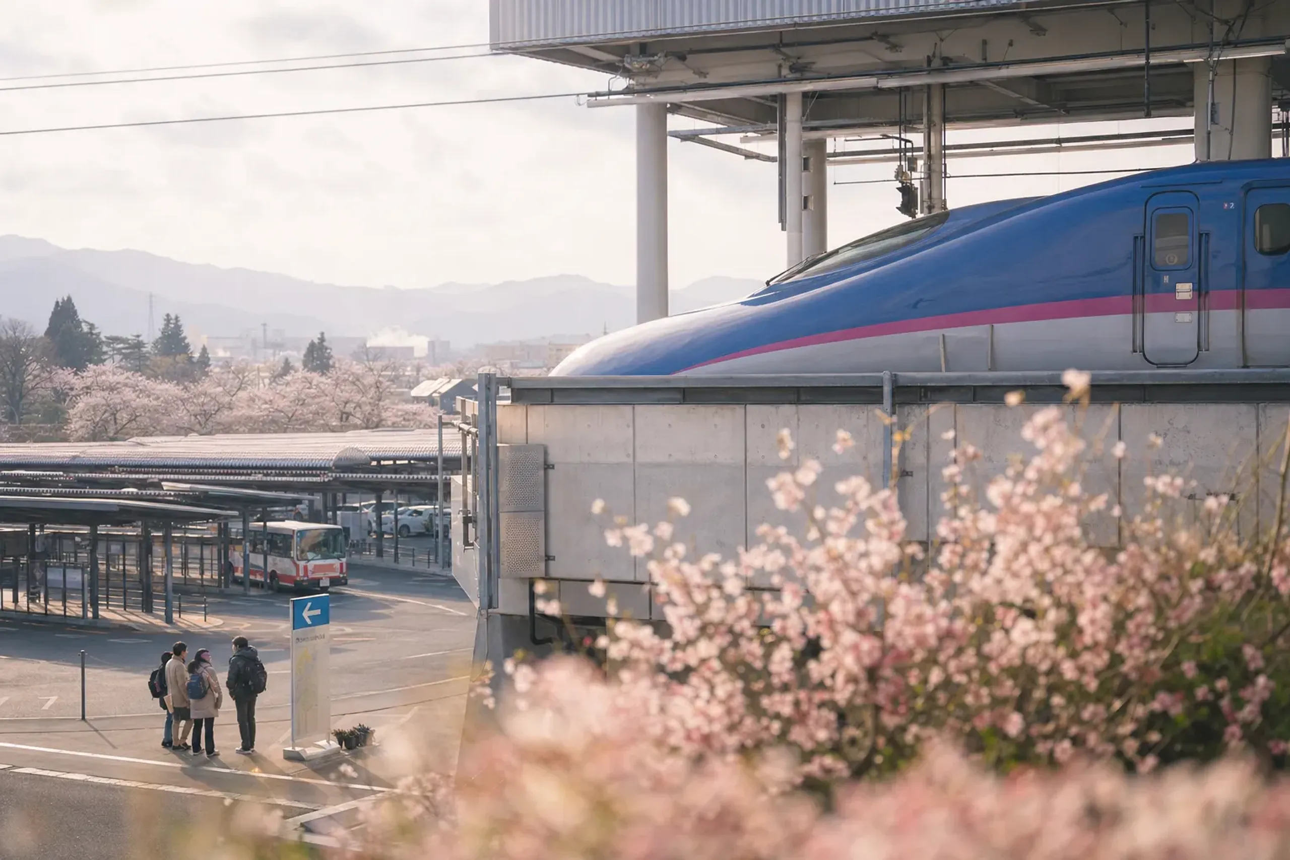 A Tohoku Shinkansen train pulling into Fukushima Station, with the station's East Exit seasonal bus stops visible in spring