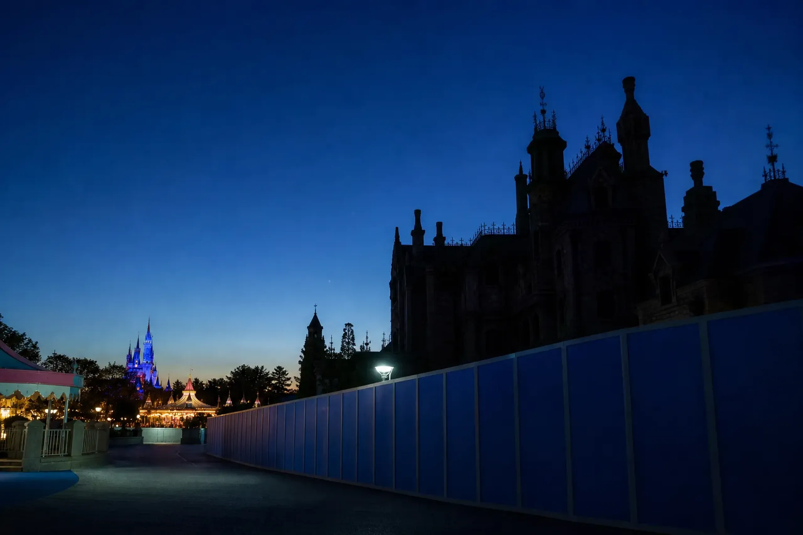 the darkened exterior facade of the Haunted Mansion attraction at Tokyo Disneyland, its Gothic mansion silhouette shuttered behind construction barriers during the seasonal overlay installation