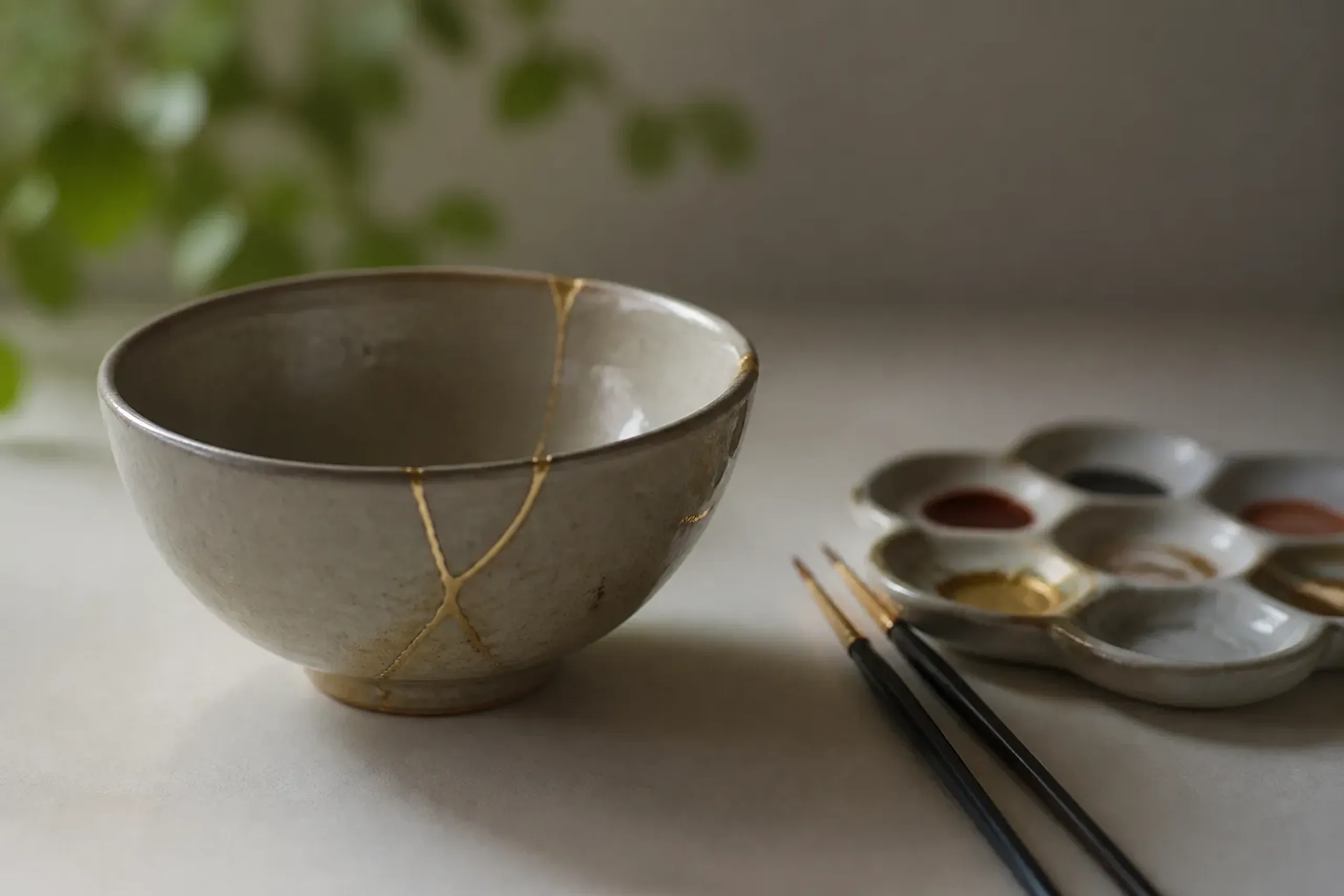 Ceramic bowl repaired with kintsugi-style gold lines beside small brushes