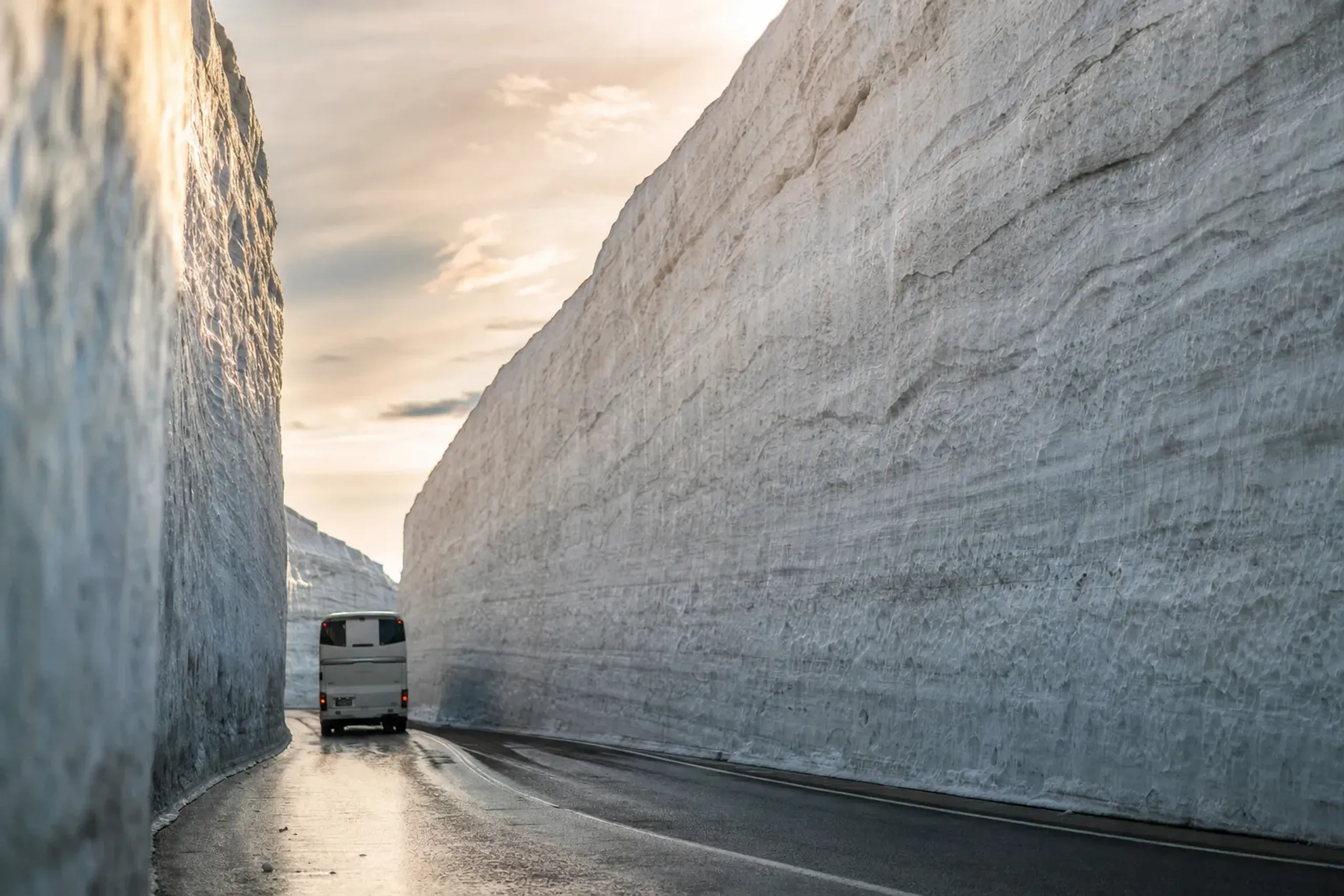 Bus driving between twenty-meter snow walls on the Tateyama Kurobe Alpine Route in mid-April