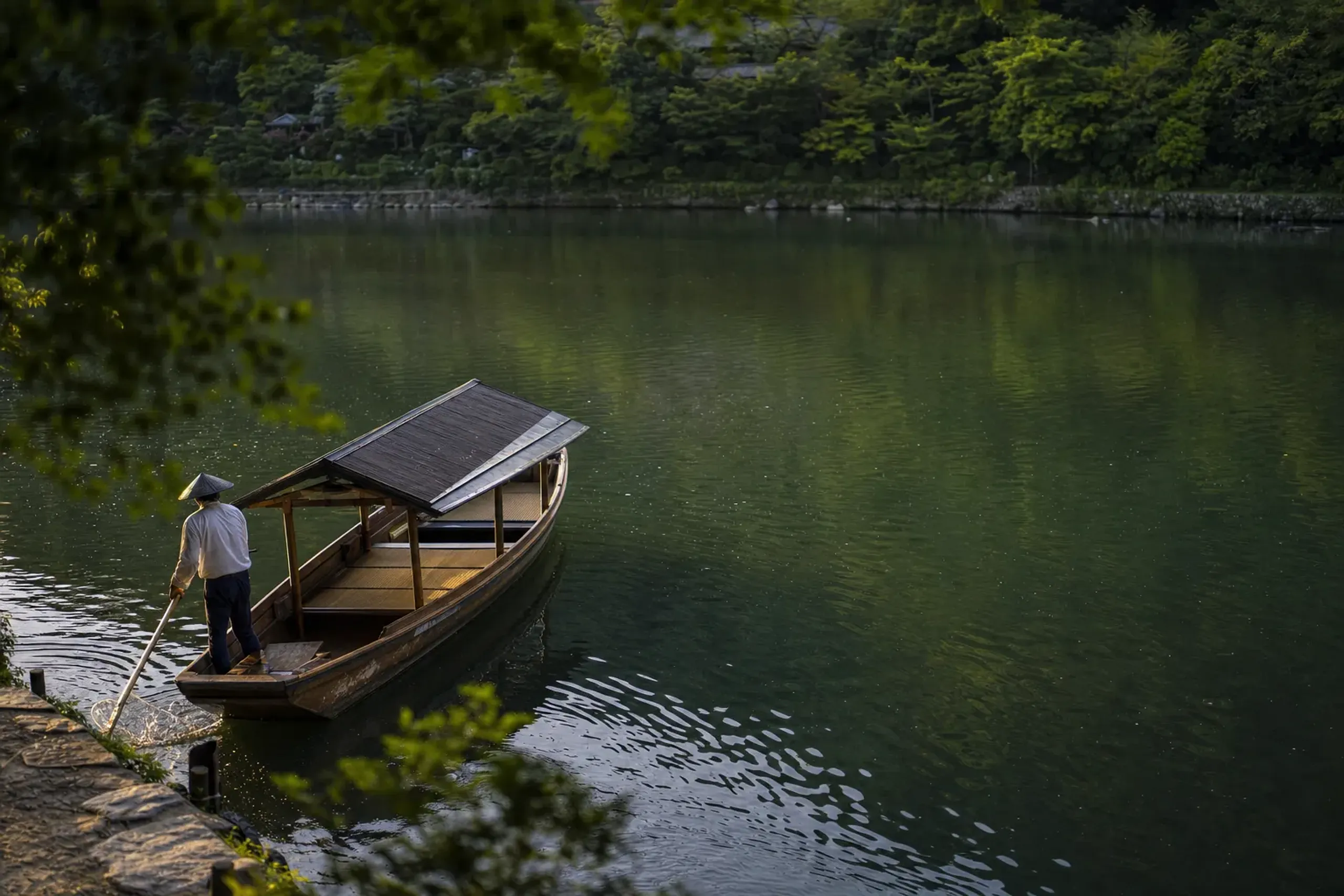 Wooden boat leaving the Togetsukyō Bridge dock in Arashiyama for the river approach to HOSHINOYA Kyoto