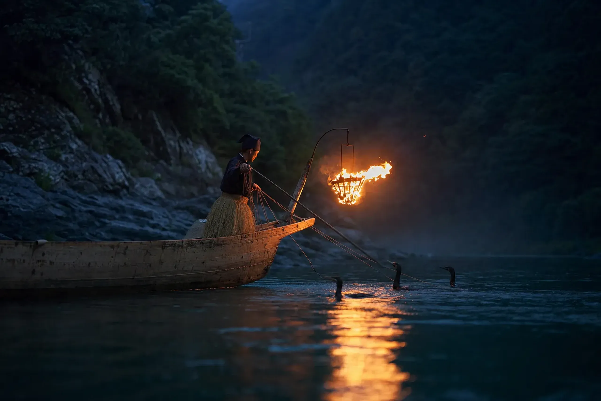 a cormorant fishing (ukai) boat on the Hozugawa River at dusk, with lit braziers and cormorants near the water during the seasonal private ukai viewing
