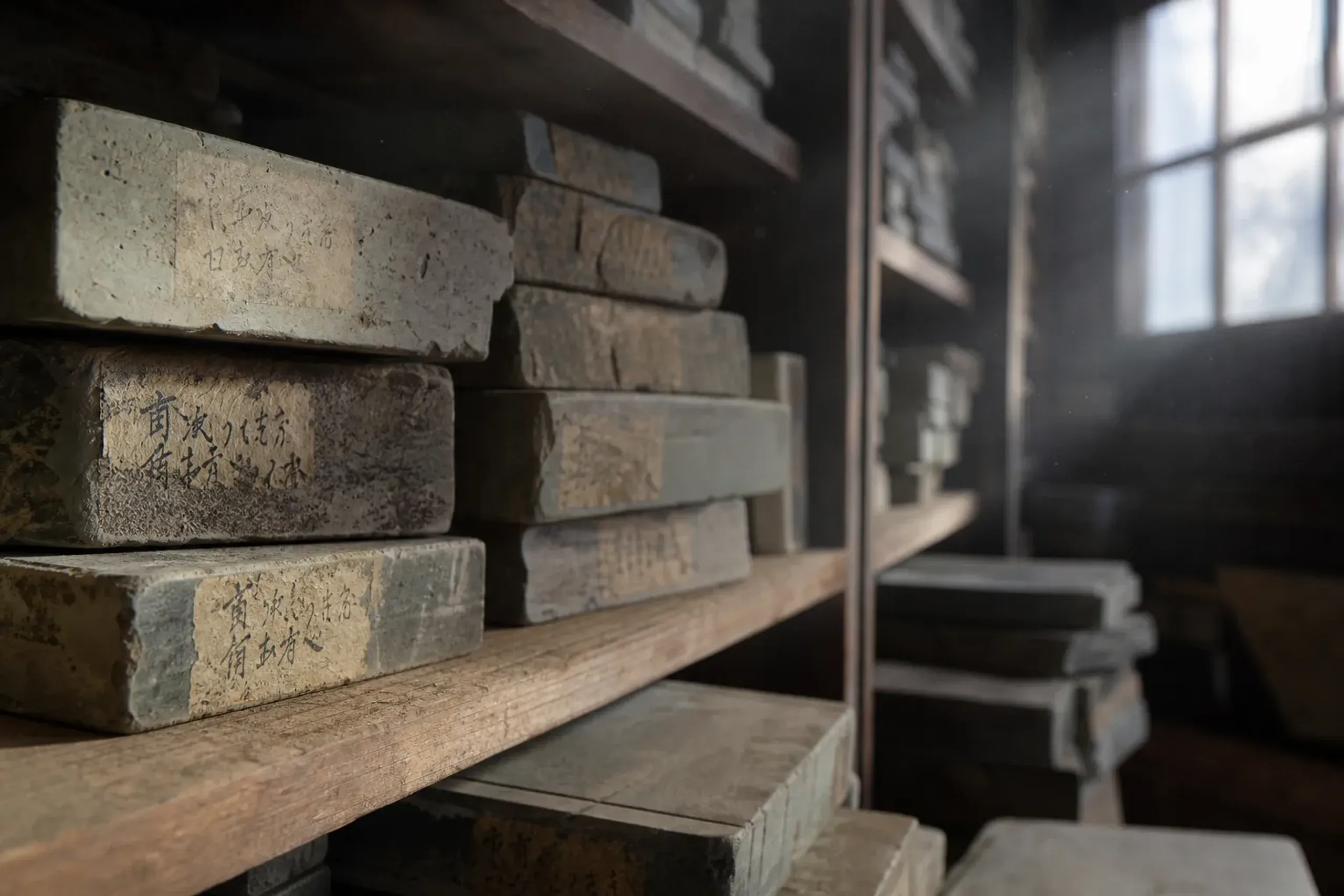 A guarded legacy stock of aged natural whetstones from exhausted historic Kyoto quarries, stacked and labeled on wooden shelves