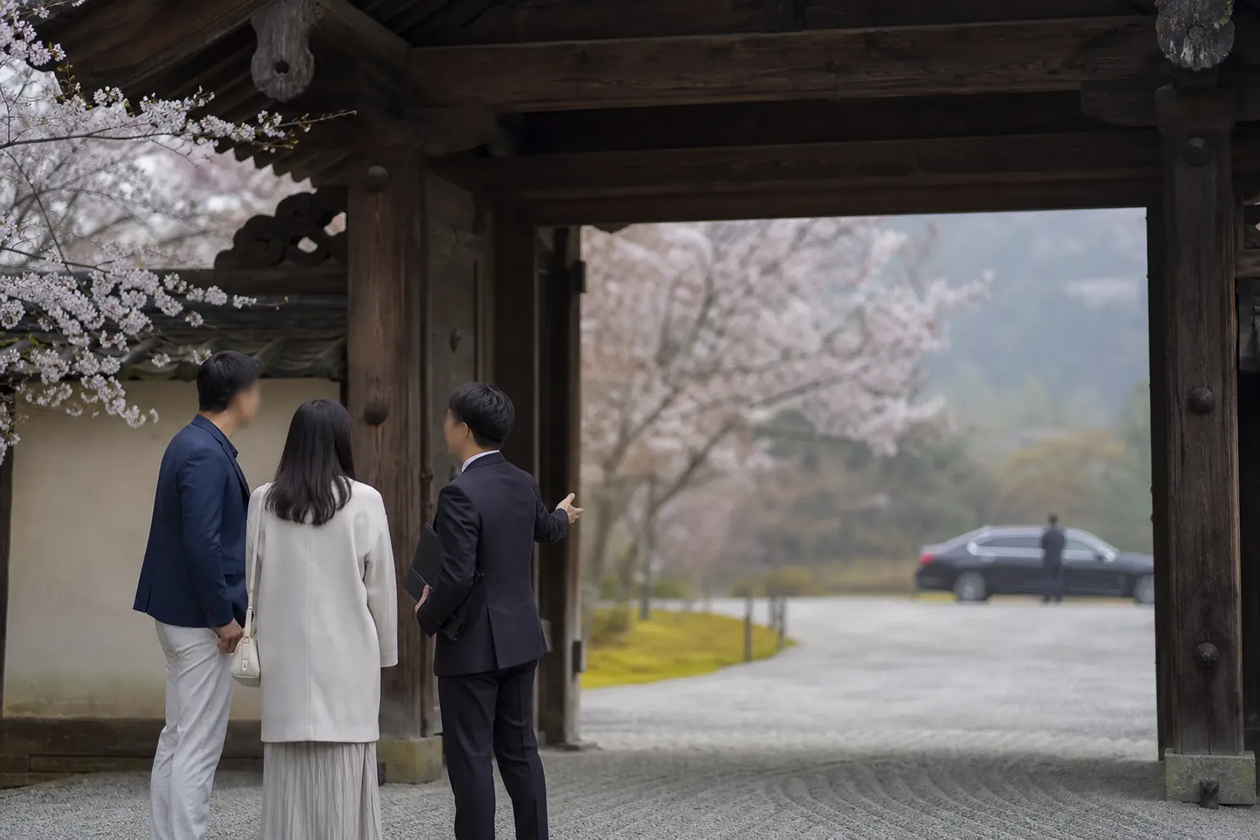 Guide briefing guests before entering a Kyoto temple precinct while a vehicle waits separately