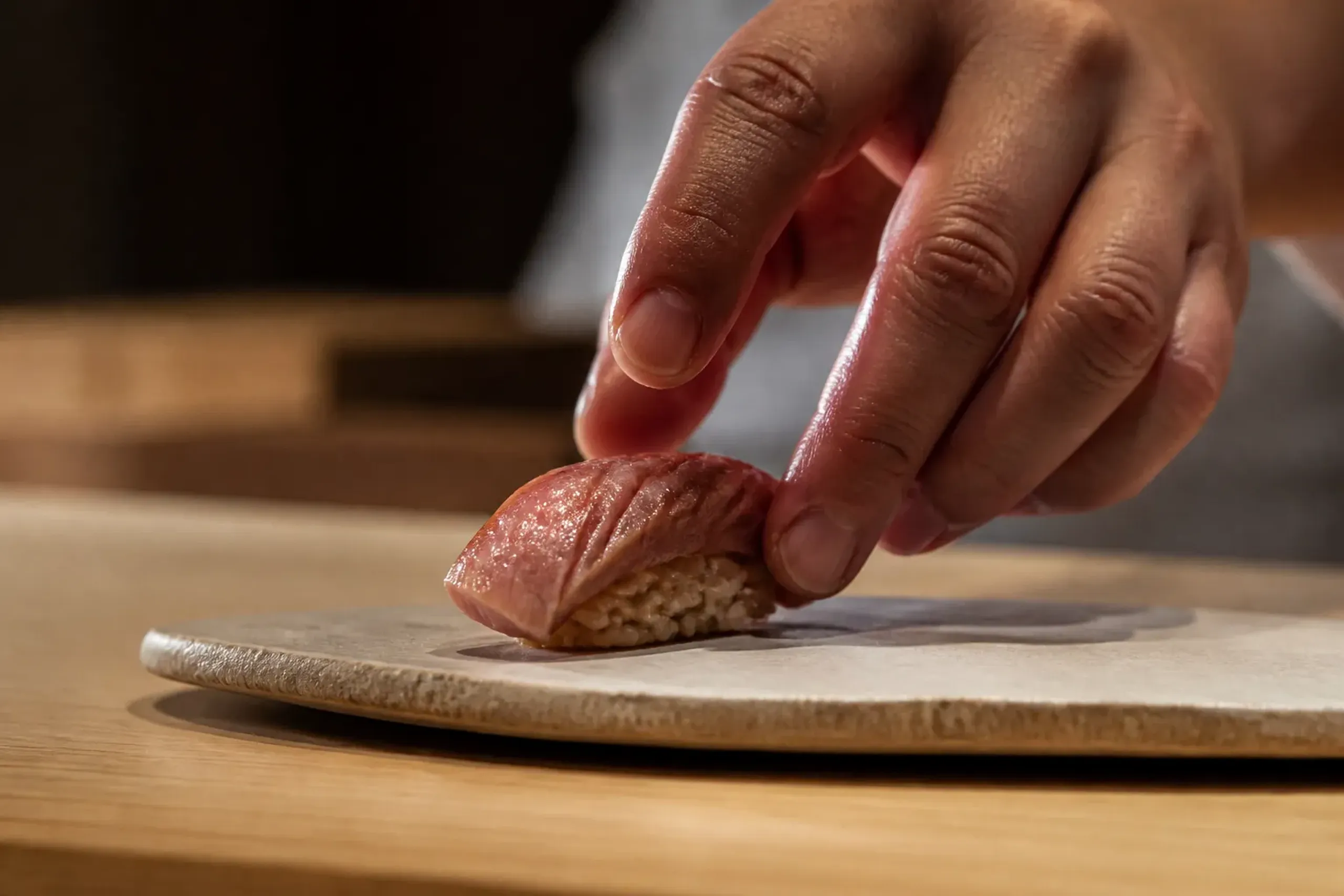 Chef placing sushi on a simple ceramic plate at a wooden counter