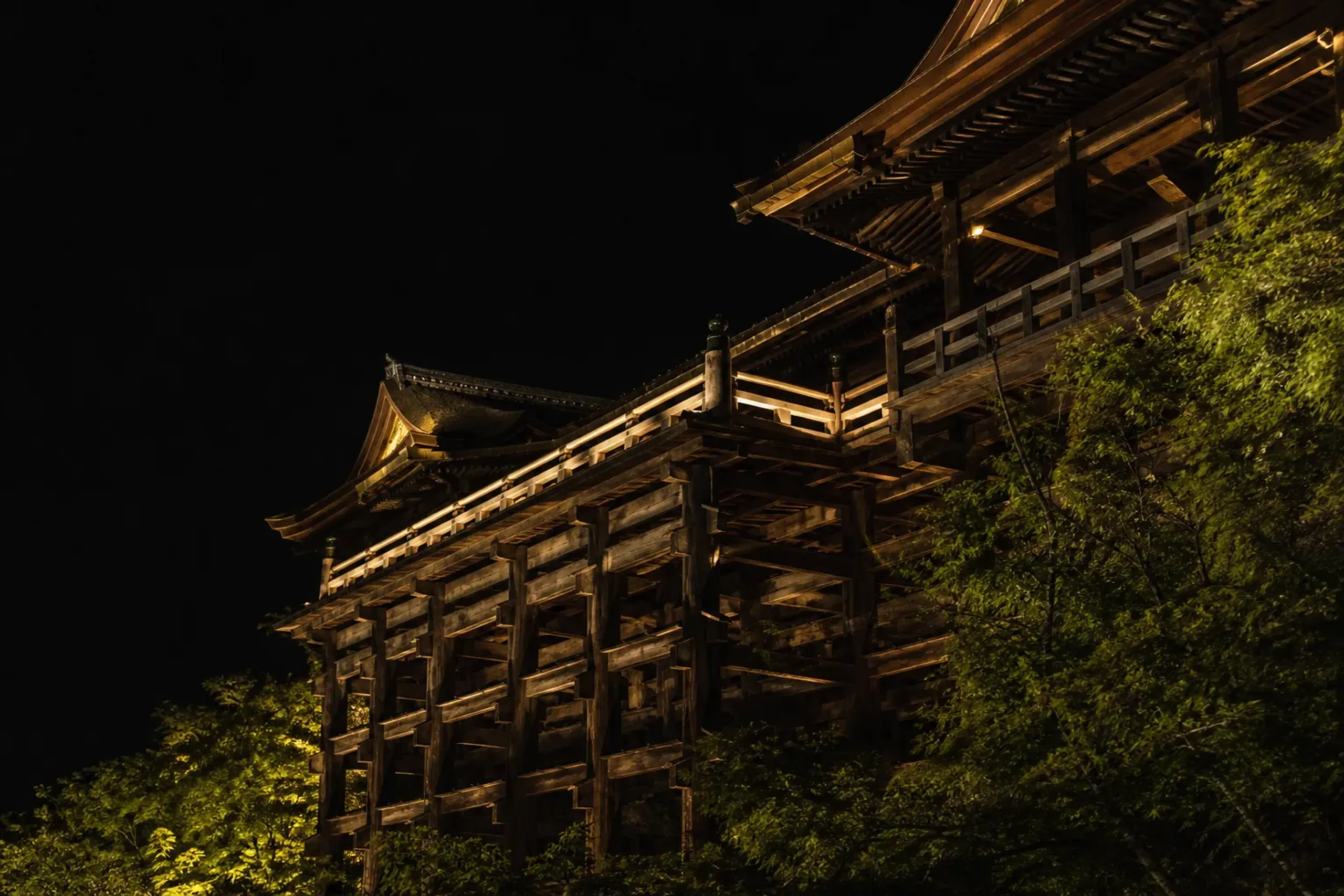 Kiyomizu-dera at night with lantern light illuminating wooden architecture and rooflines