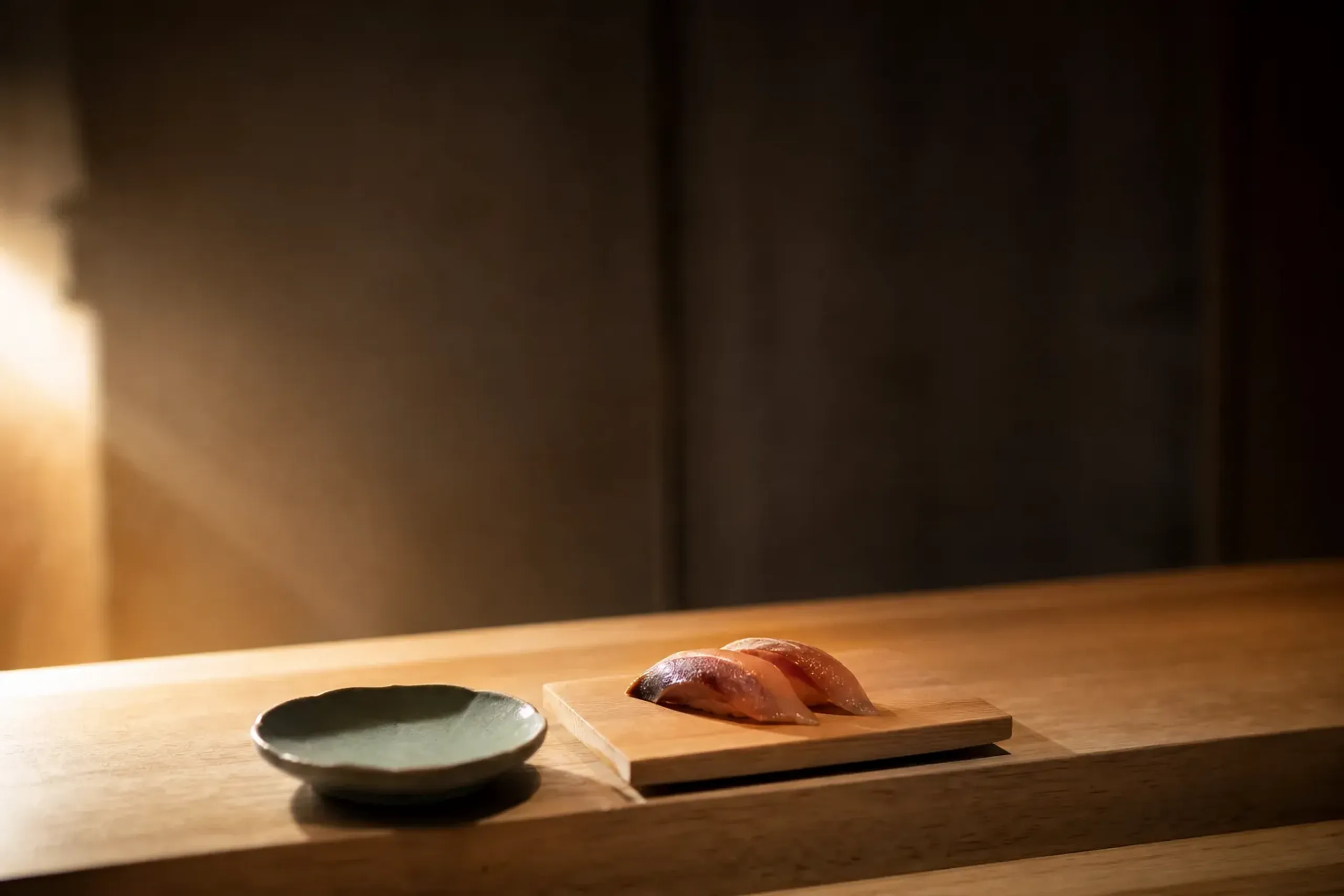 Minimalist sushi counter place setting with ceramic dish and seasonal fish on a wooden board
