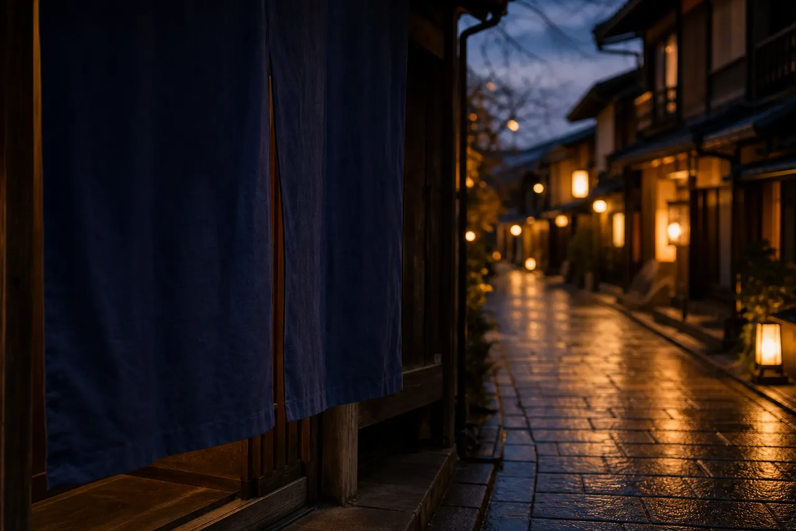 A dark indigo noren curtain hanging in a dim Gion lane doorway at the edge of dusk, with softly dimming shopfront lanterns beyond