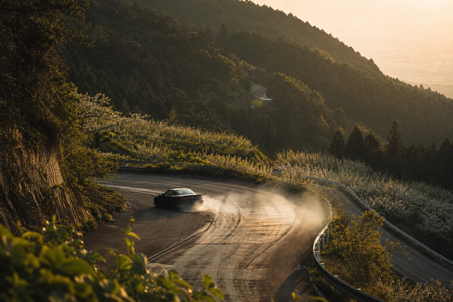 Car performing a high-speed drift on a winding mountain road, white smoke trailing the tires as it circles a hairpin turn on a forested slope.